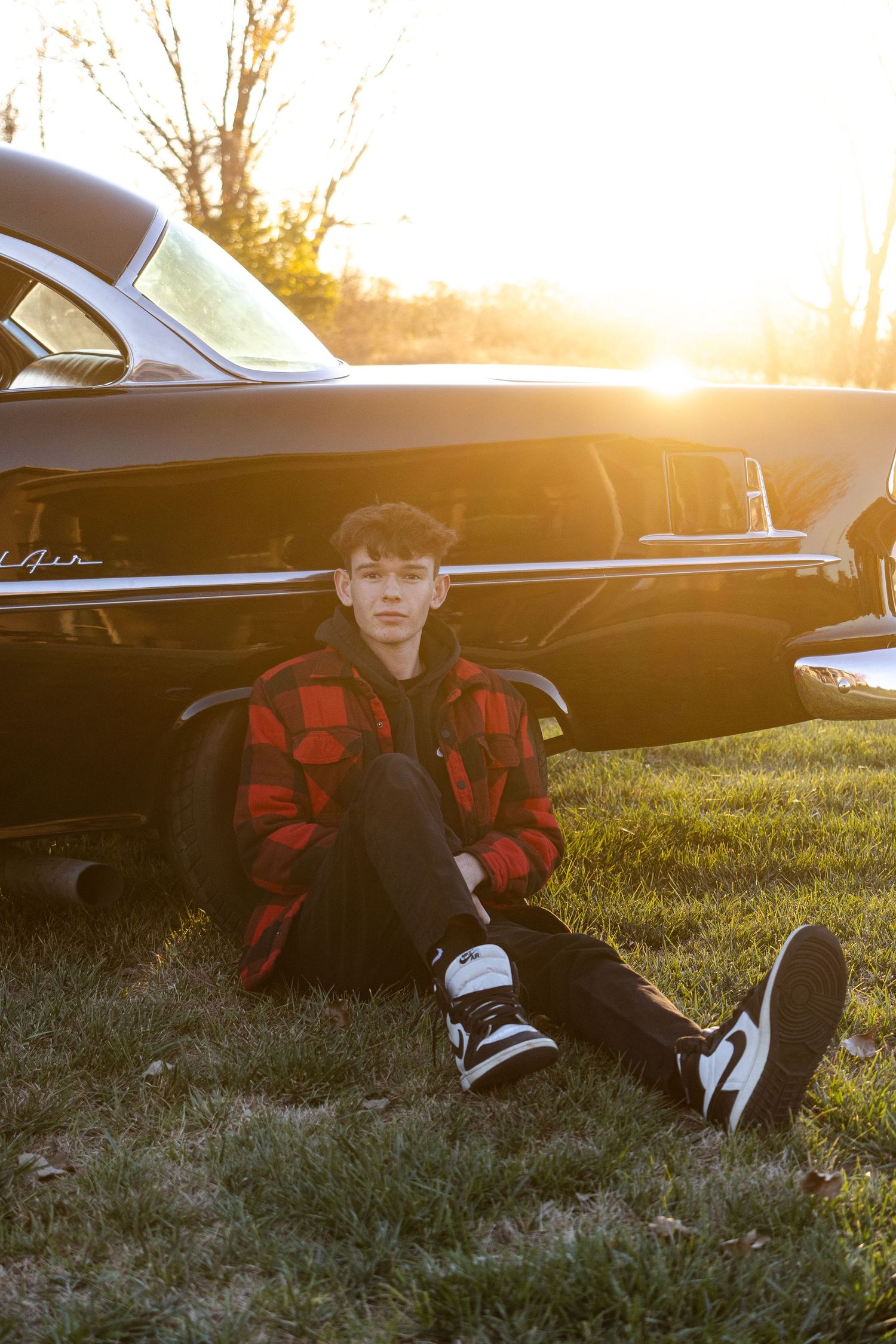 Sunset silhouette with classic car and person in red plaid jacket.