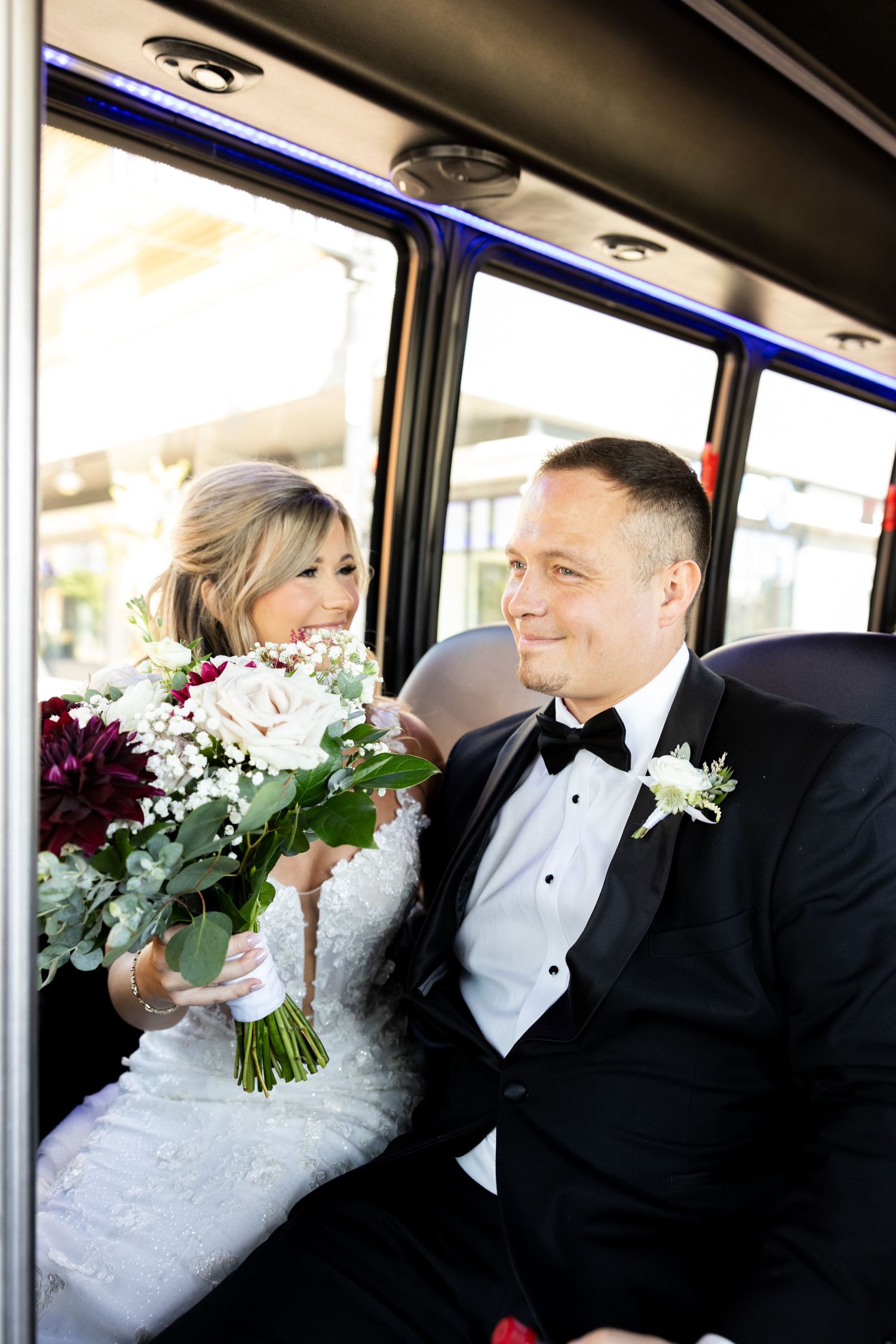Wedding party rides together in decorated bus with floral bouquets.