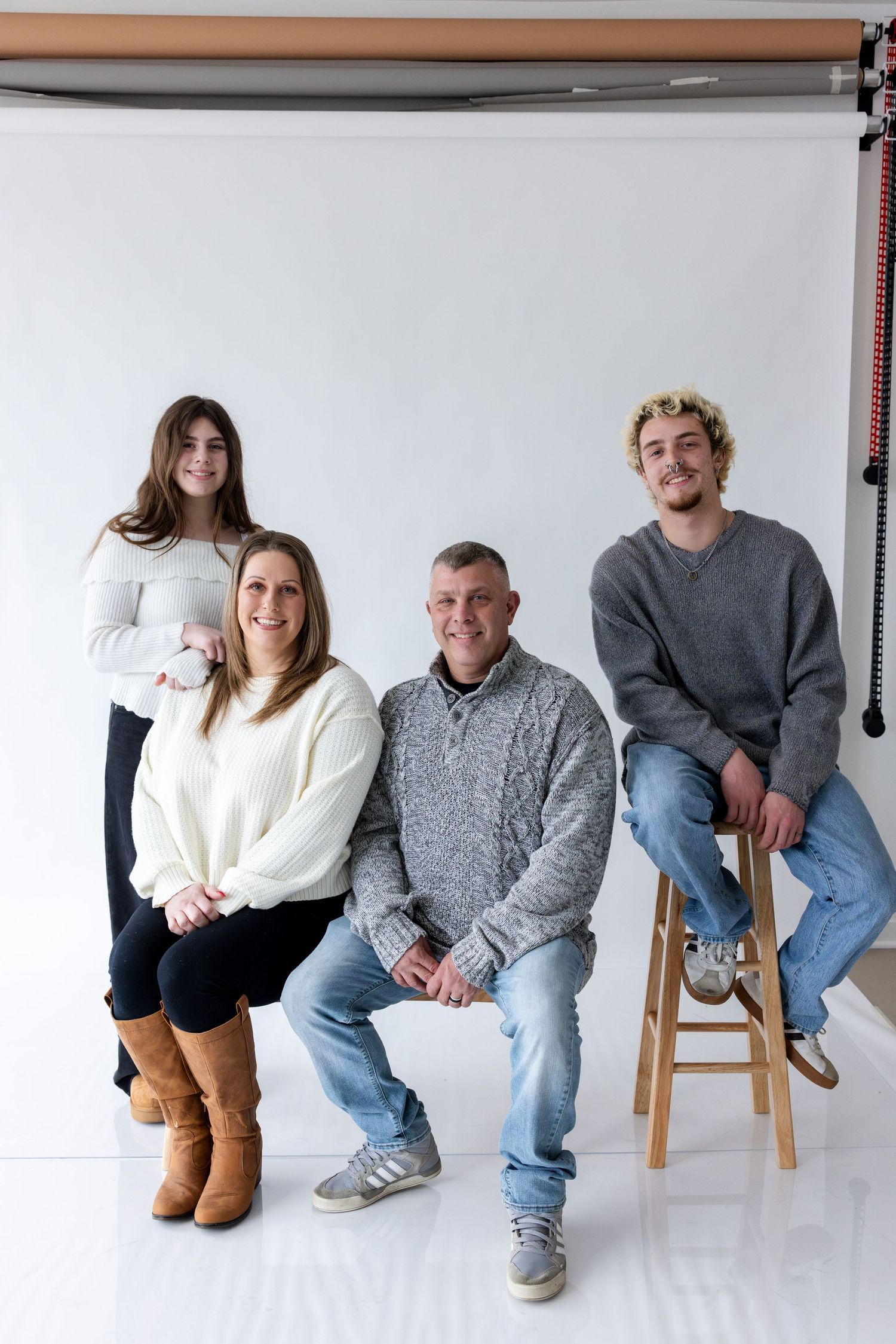 Family members sit casually together on wooden stools against a white studio backdrop.