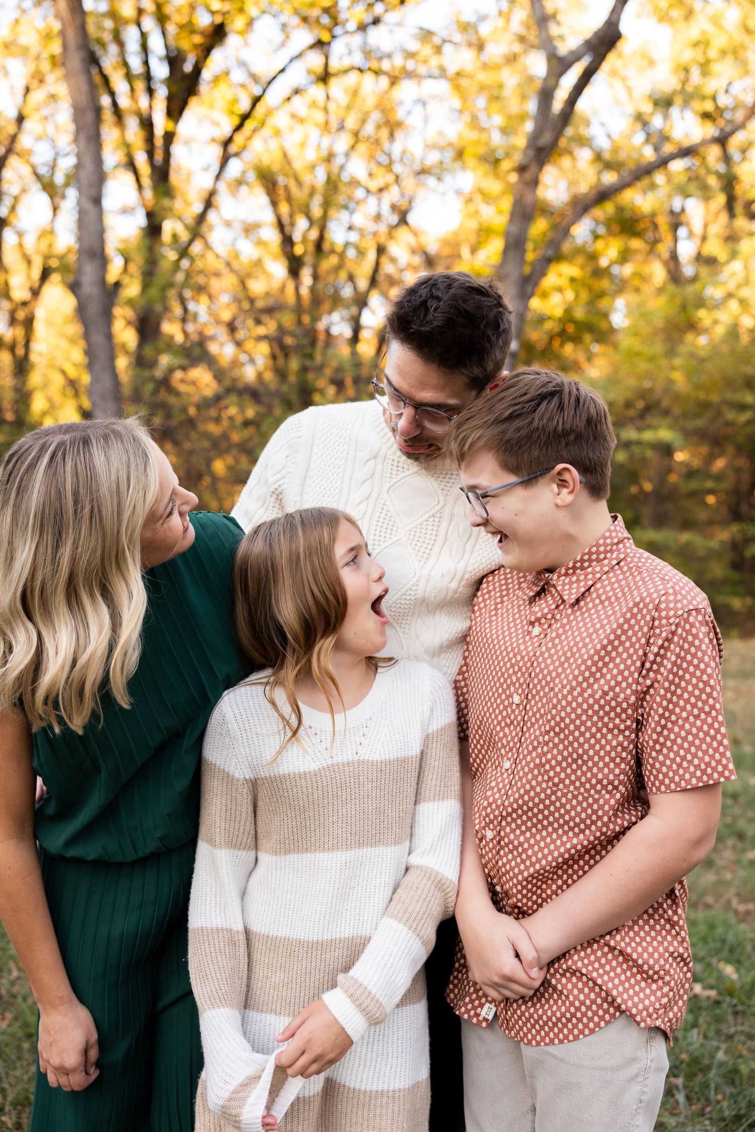 Family members share laughs together in a sun-lit autumn forest setting.