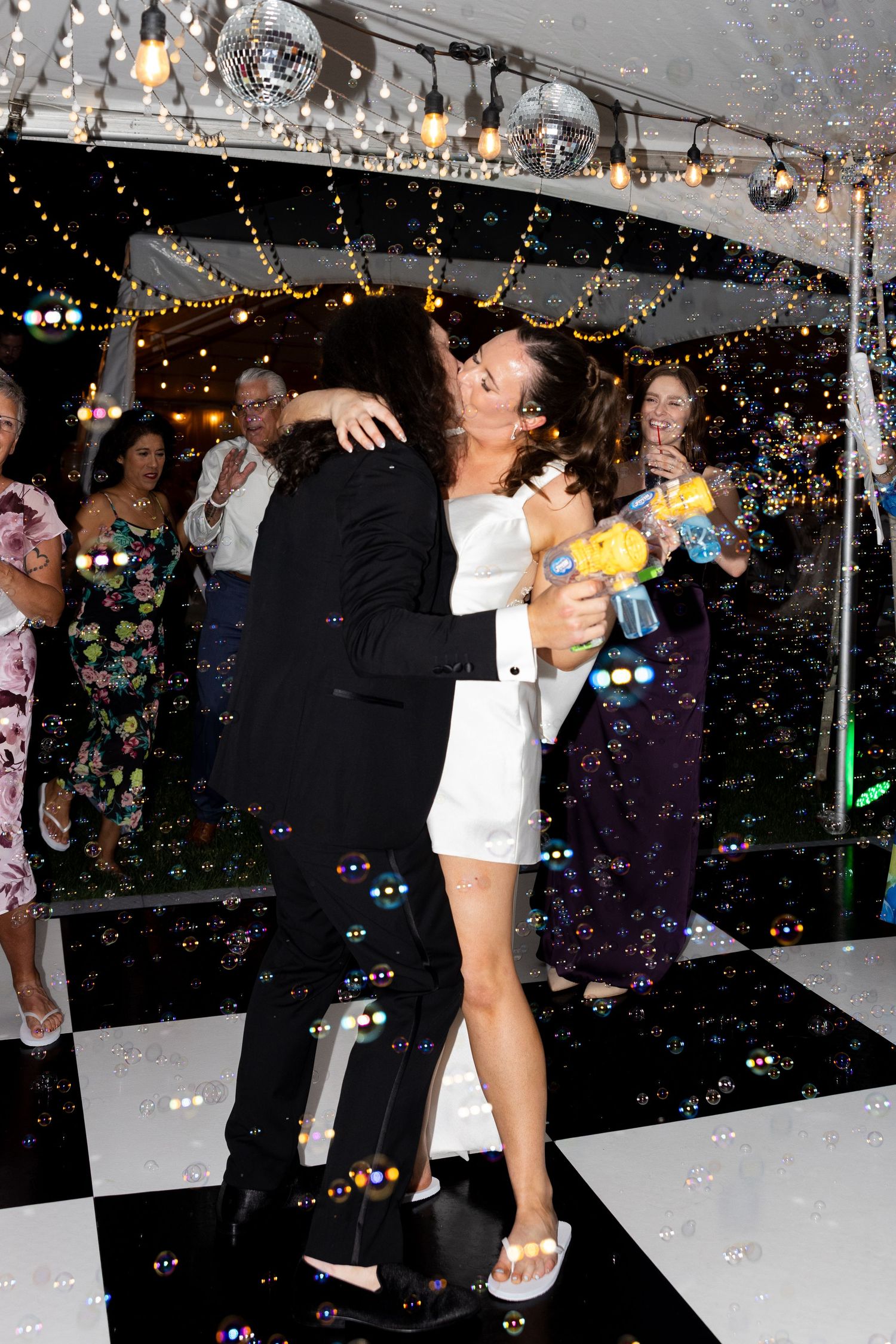 Couple sharing a romantic dance at a wedding reception with disco balls, string lights, and bubbles floating around them.