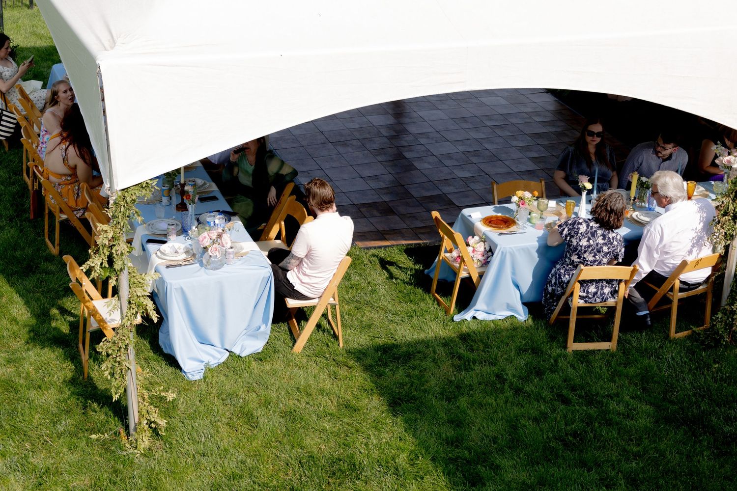 White outdoor party setup with chairs and tables arranged on grass under hanging sheets.