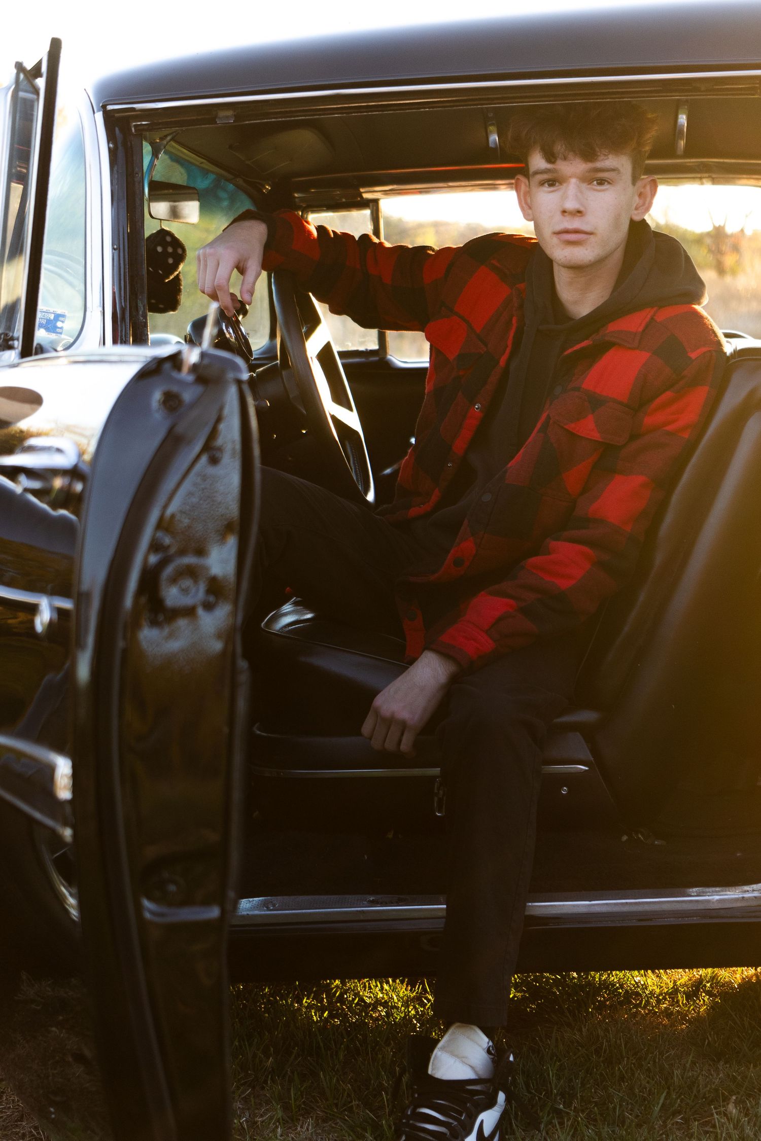 Person wearing red plaid jacket sitting in vintage car interior at sunset.