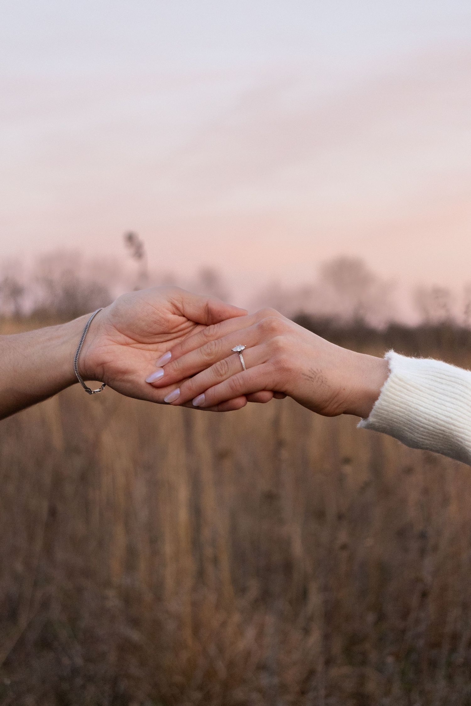 Close-up of hands reaching for each other against a sunset backdrop in a field.