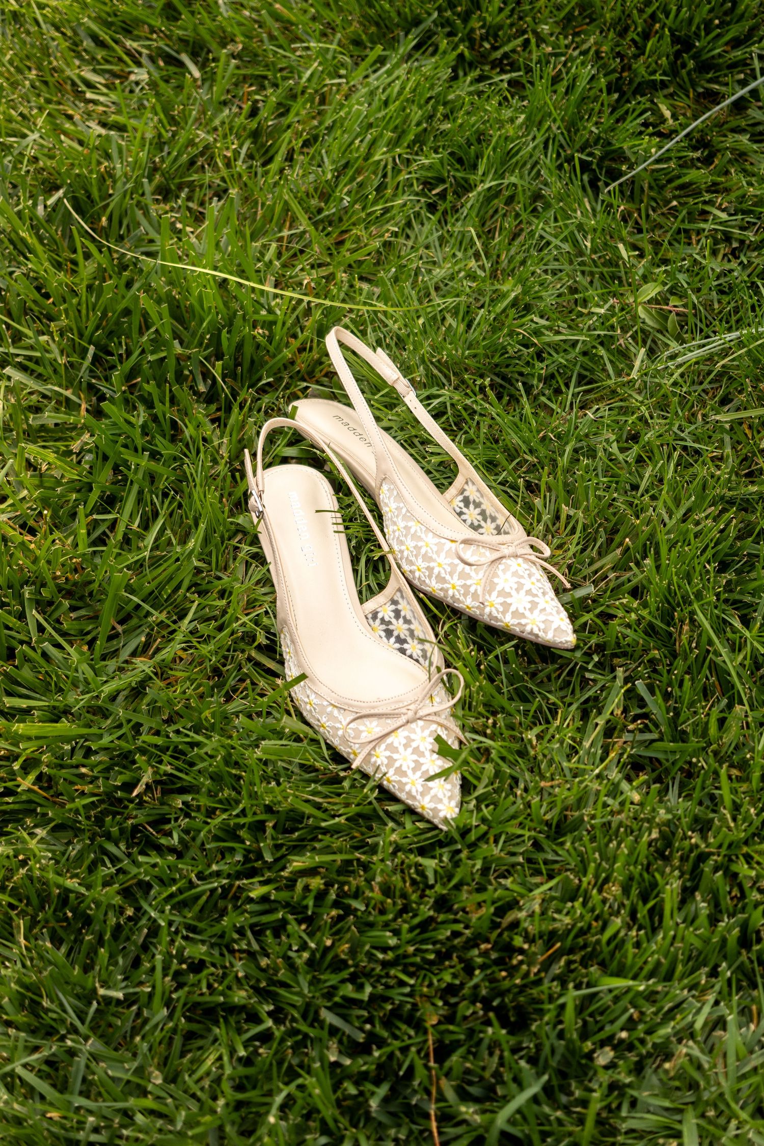White bridal shoes rest on lush green grass in a garden setting.
