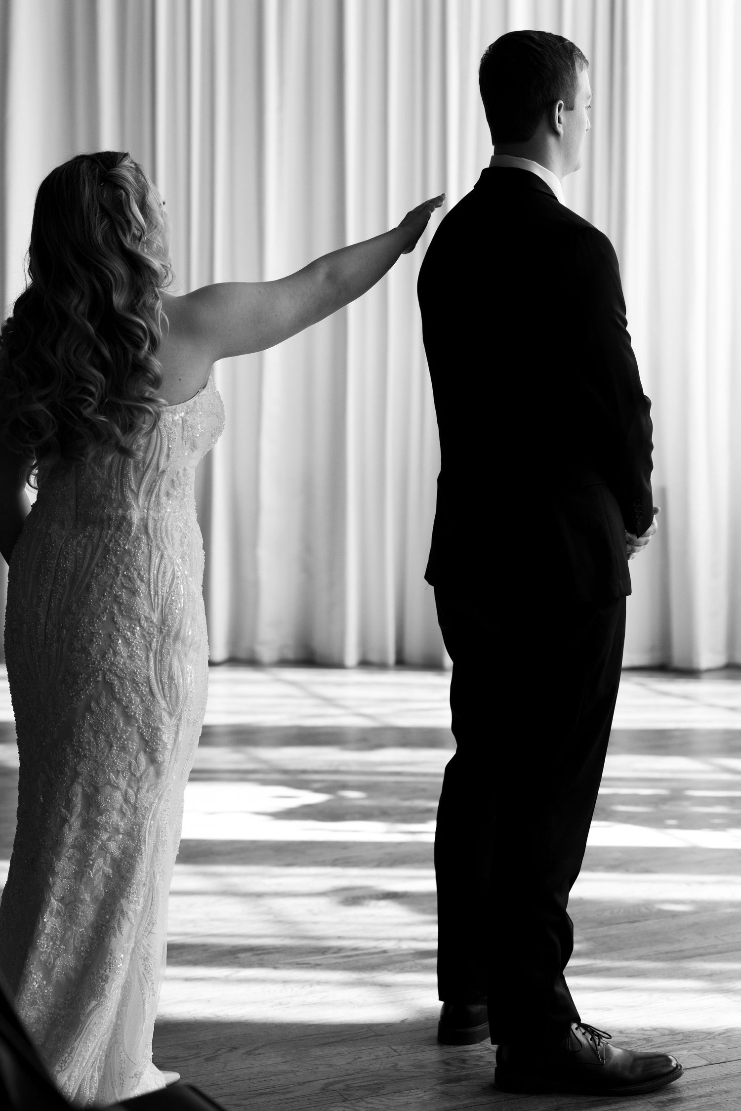Black and white photo of bride touching groom's shoulder during first look wedding moment.
