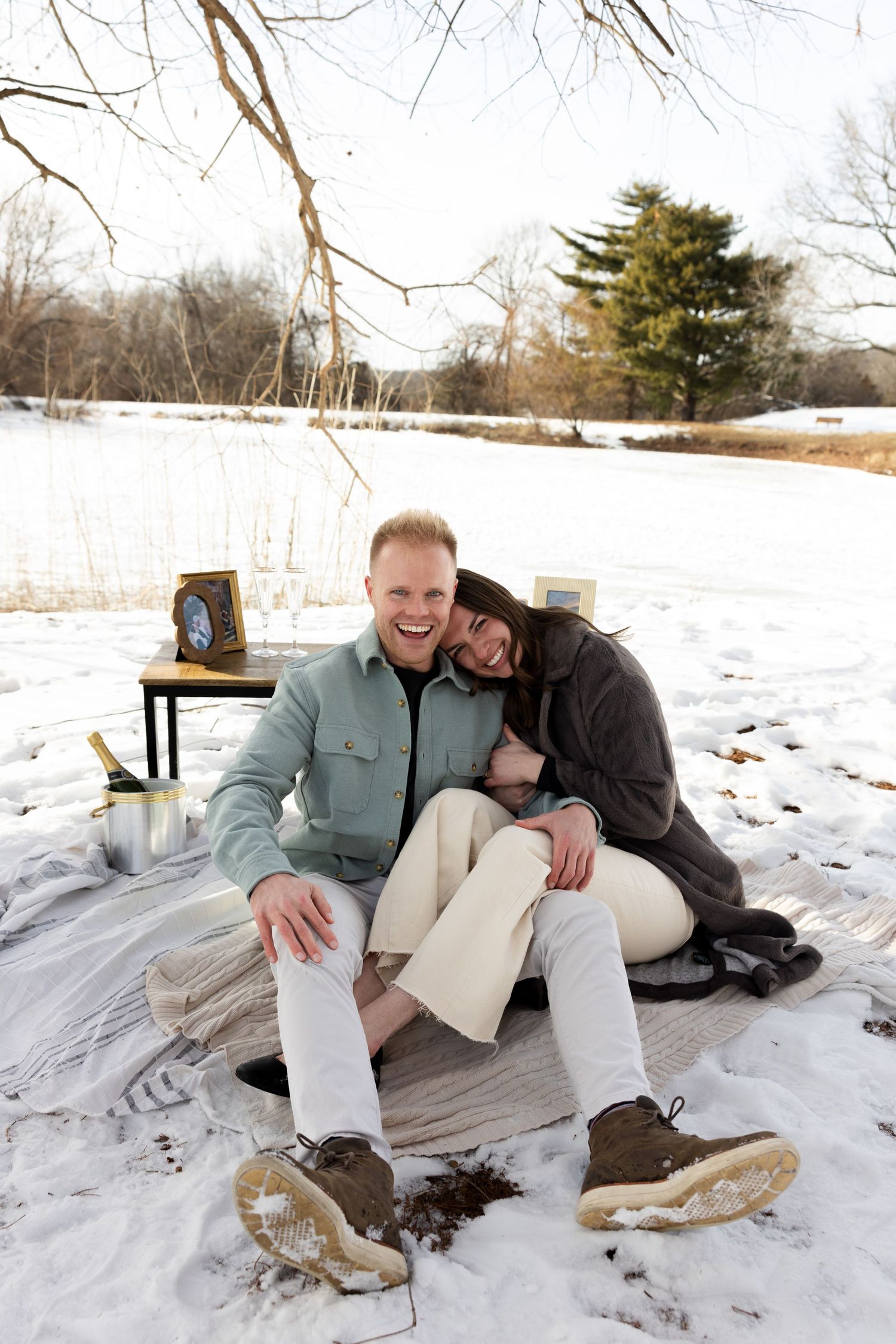A couple sits together on a snowy ground with their dog in a winter outdoor setting.