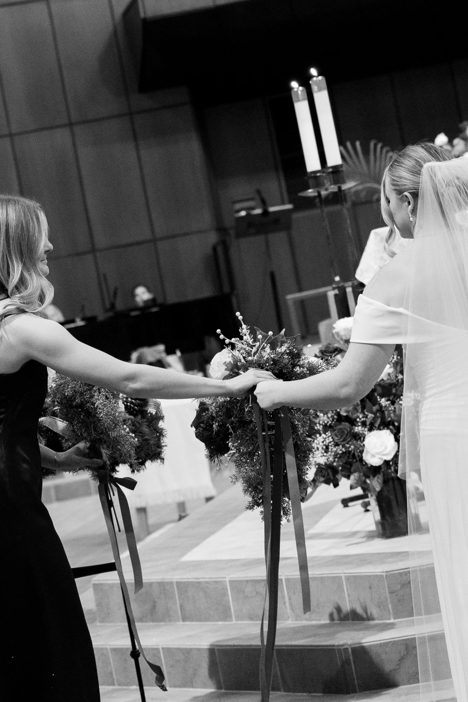 A black and white photo showing hands reaching for wedding flowers on church steps.