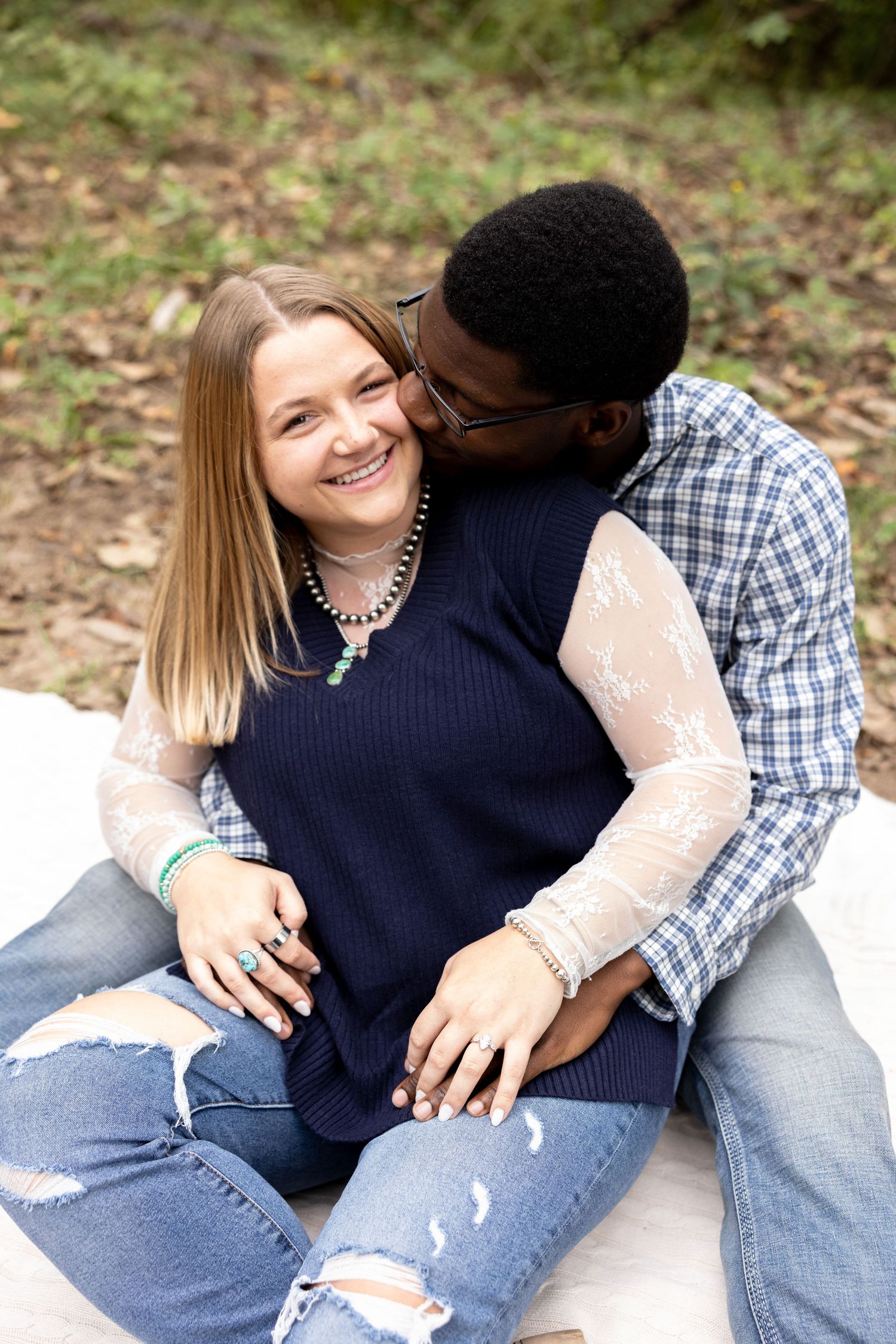 Couple snuggling intimately together while sitting outdoors in casual attire embody sweet engagement moments.