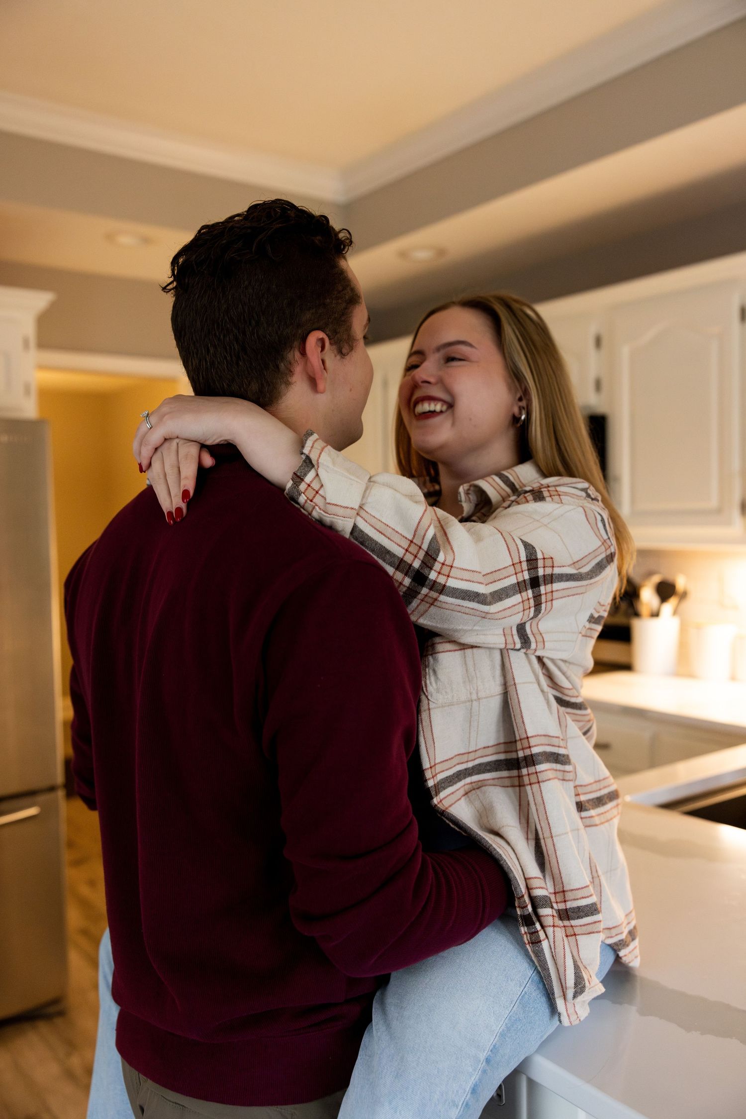 A romantic couple embraces and laughs together in a bright kitchen setting.