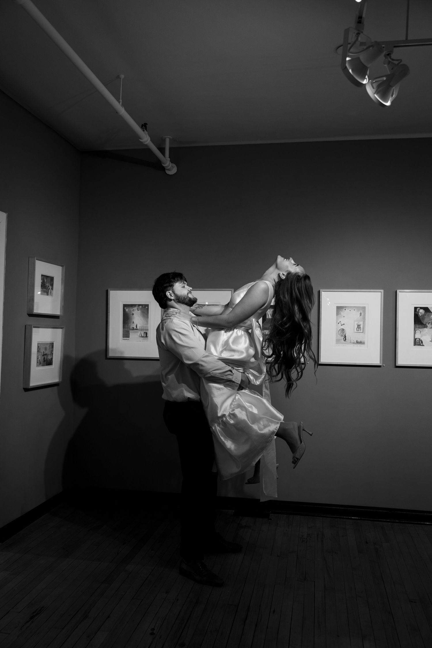 Black and white photo of a groom lifting his bride in a wedding dance inside an art gallery.