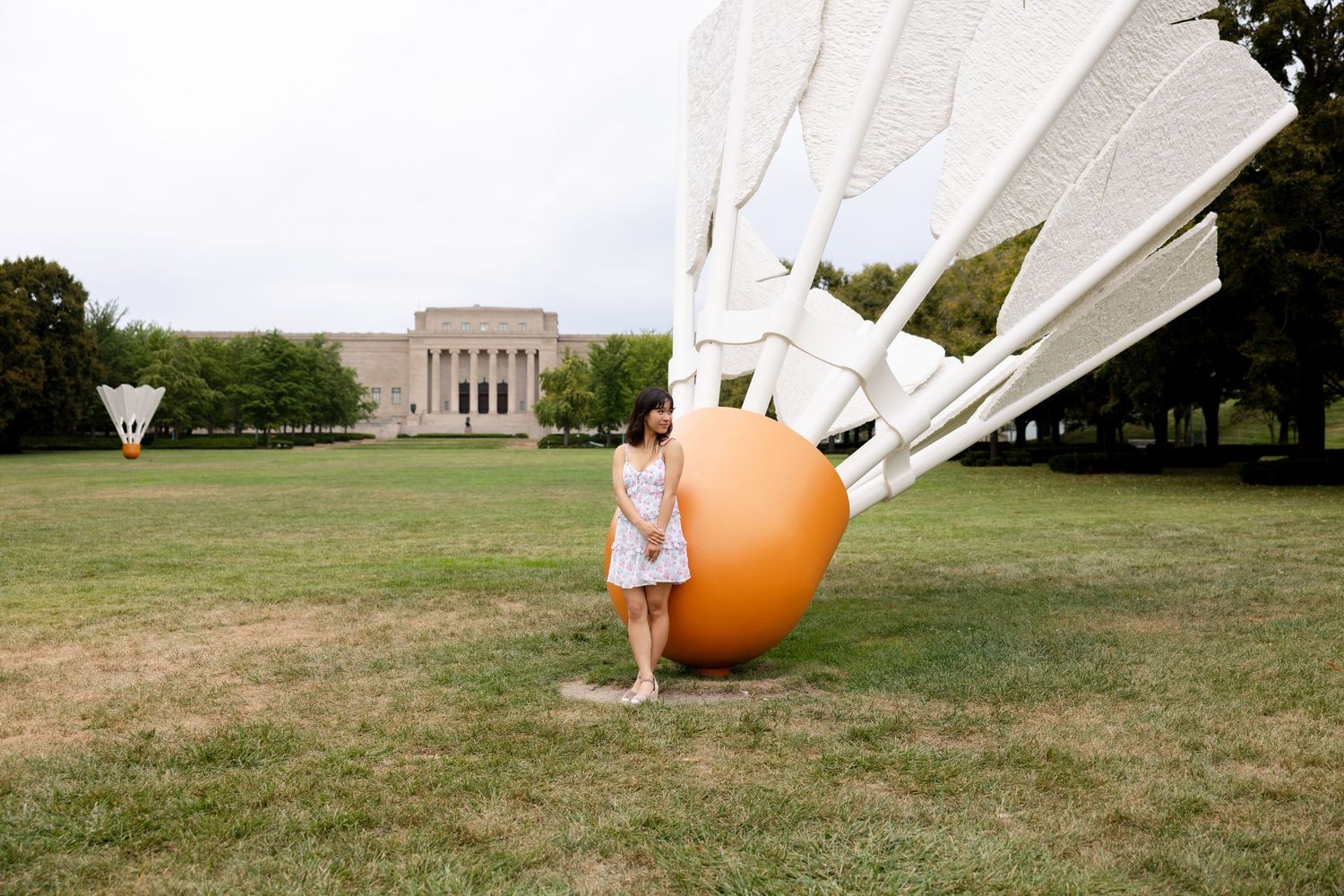 White fabric installation and orange balloon displays on a grassy field with a monument in background.