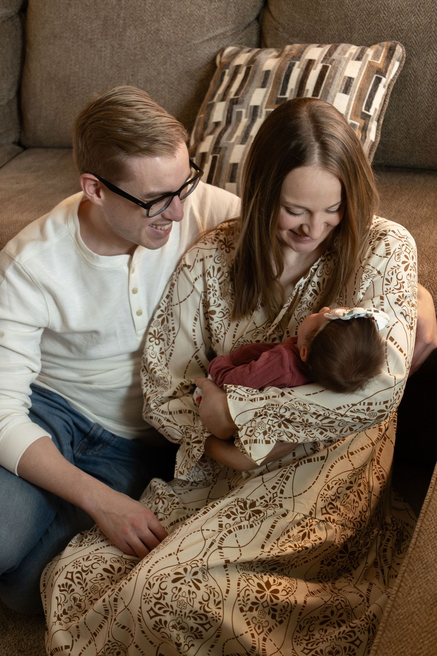 A cozy family moment on a brown sofa with decorative pillows and warm lighting.