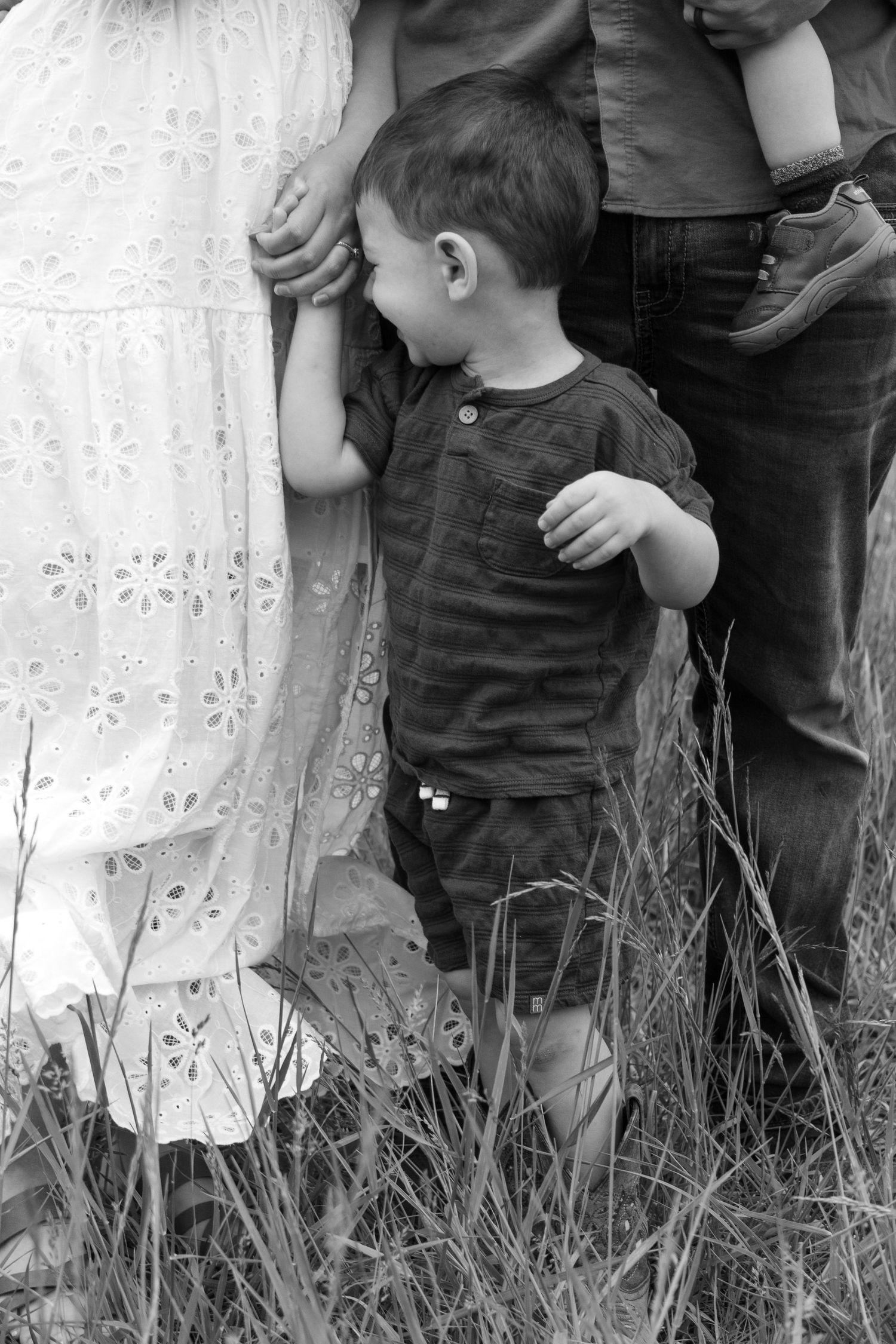 A family stands together in tall grass wearing casual summer clothing.