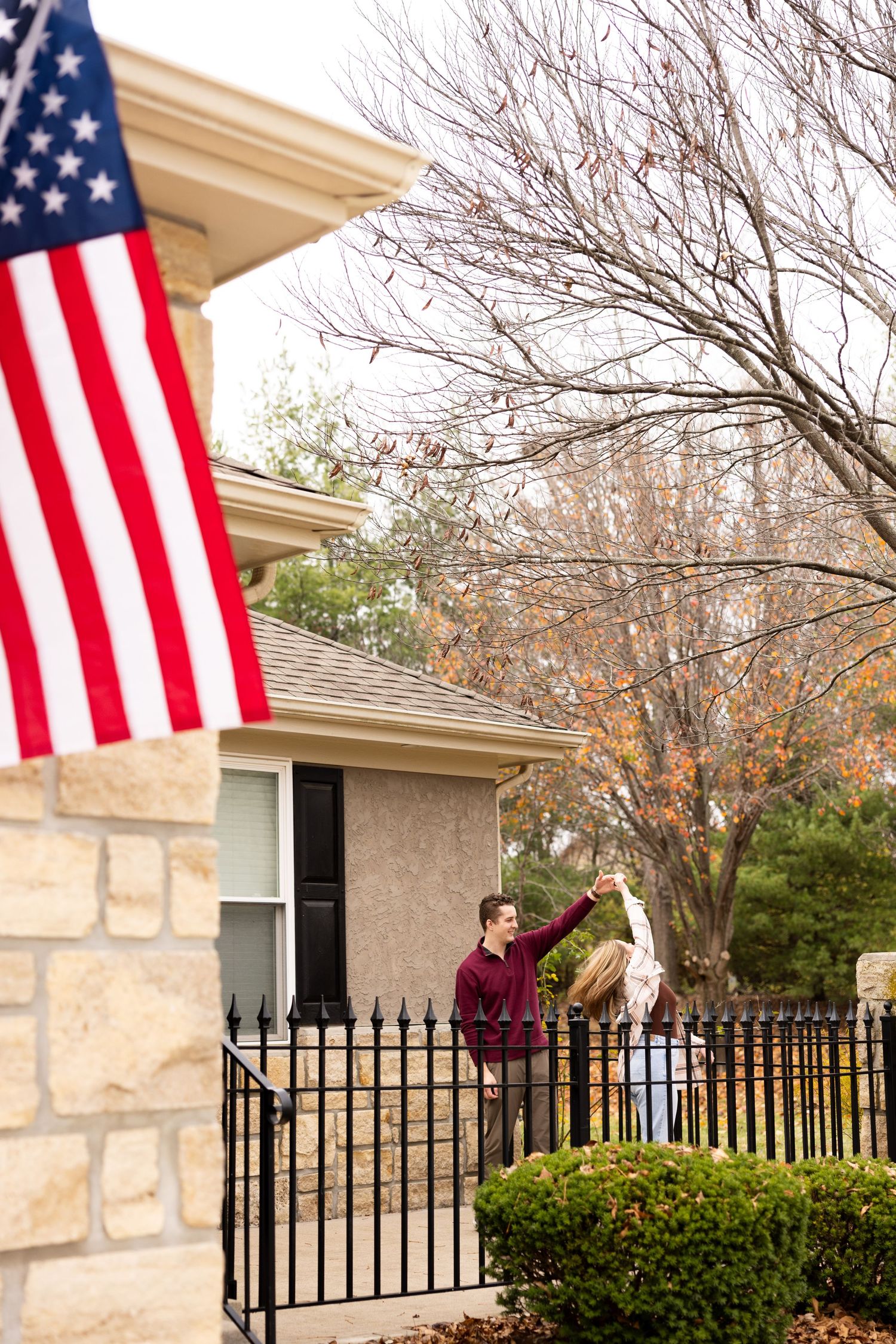 American flags wave outside a stone-accented house on a fall day.