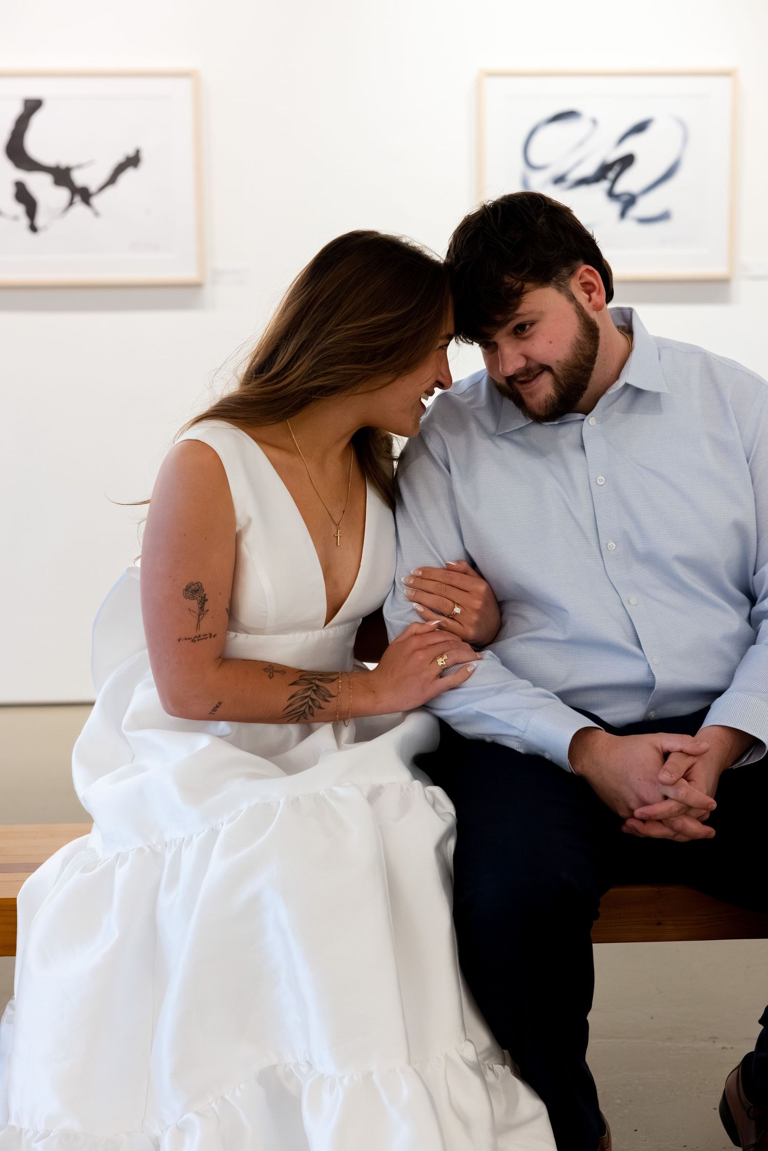 A couple shares an intimate moment while sitting on a bench in an art gallery with abstract paintings on the wall.