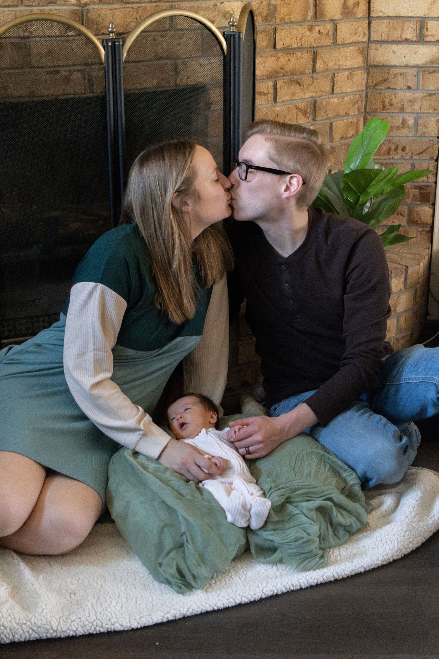 Tender family moment shared on a white carpet against brick wall backdrop.