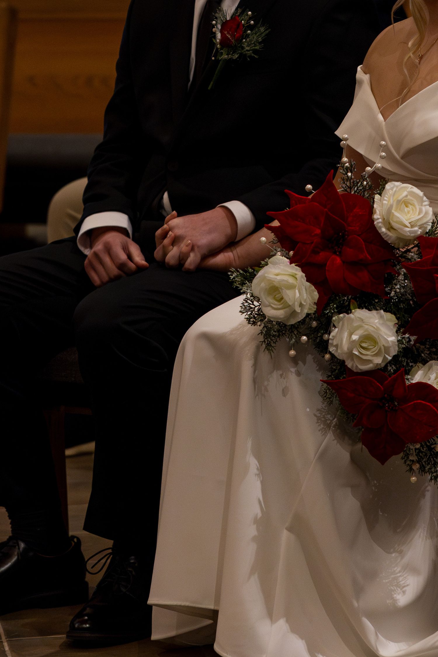 A close-up view of a wedding couple sitting together with red and white roses in their formal attire.