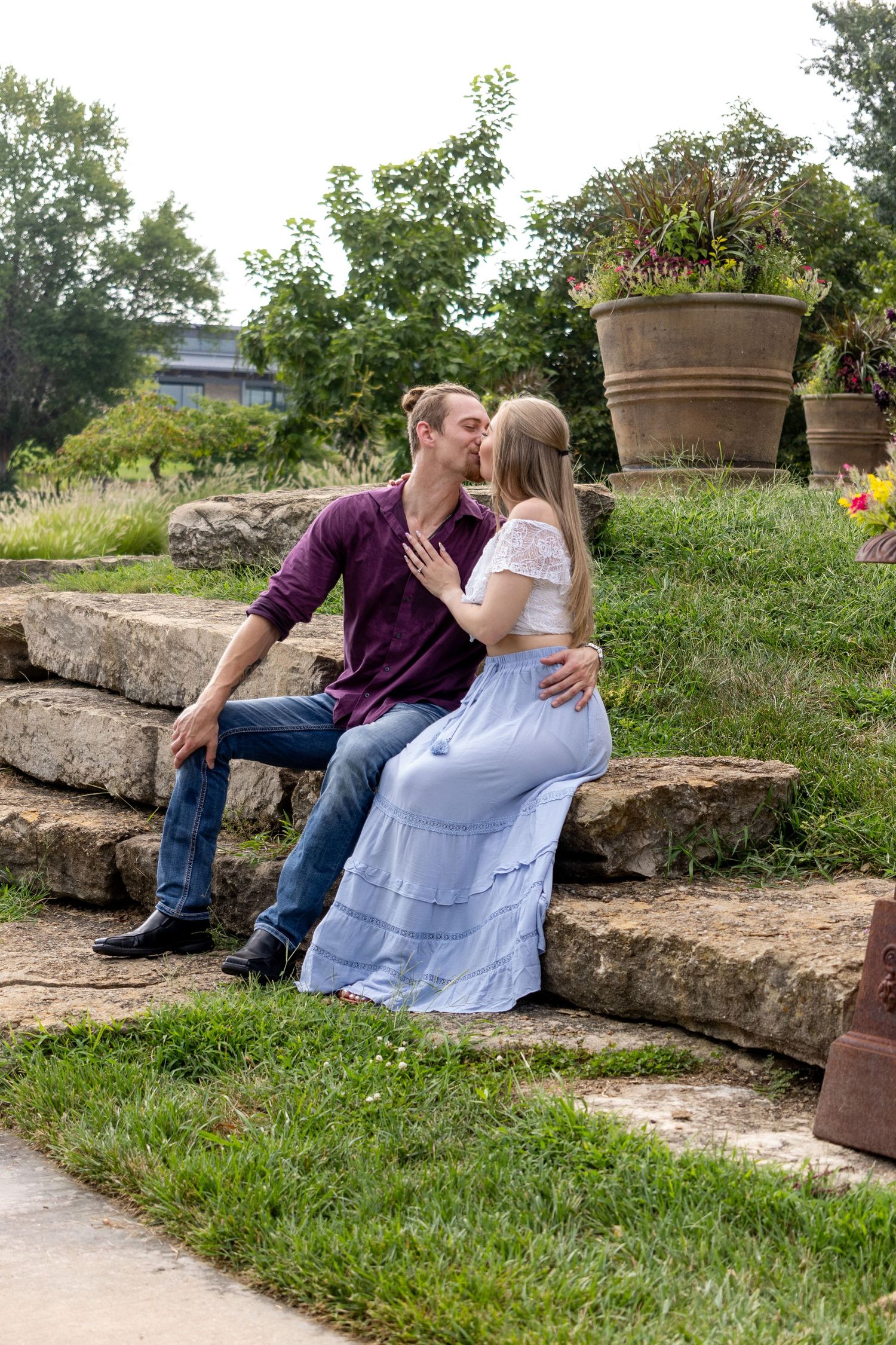 A romantic moment shared between a couple sitting on stone steps in a garden setting.