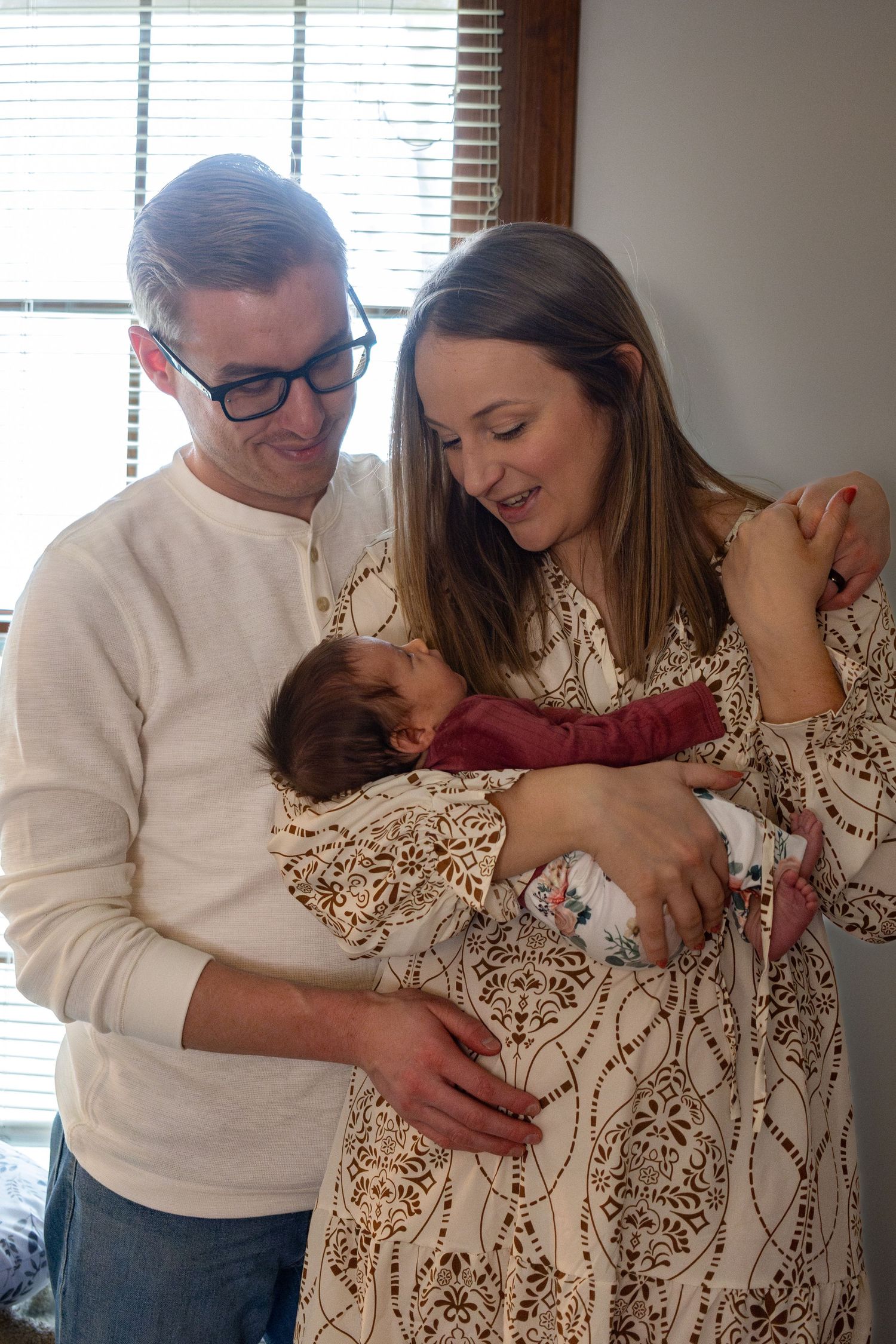 A tender family portrait by a window showing gentle moments with a newborn.