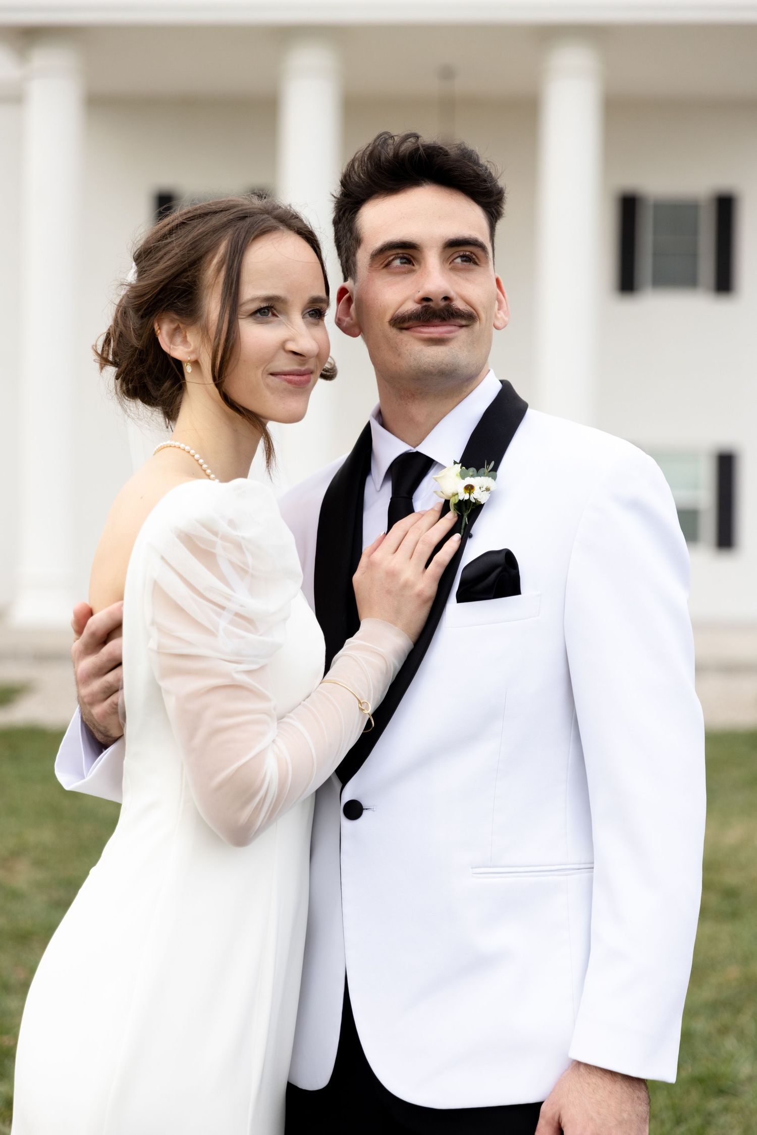 Elegant couple poses in formal wedding attire in front of a white columned building.