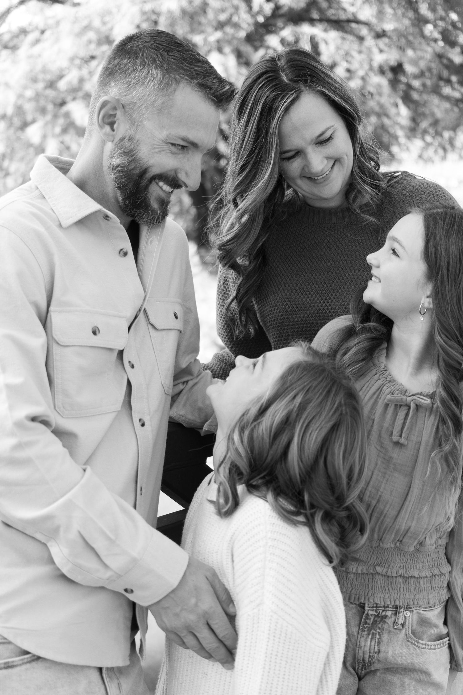 Family shares candid laughing moment together during black and white outdoor photo session.