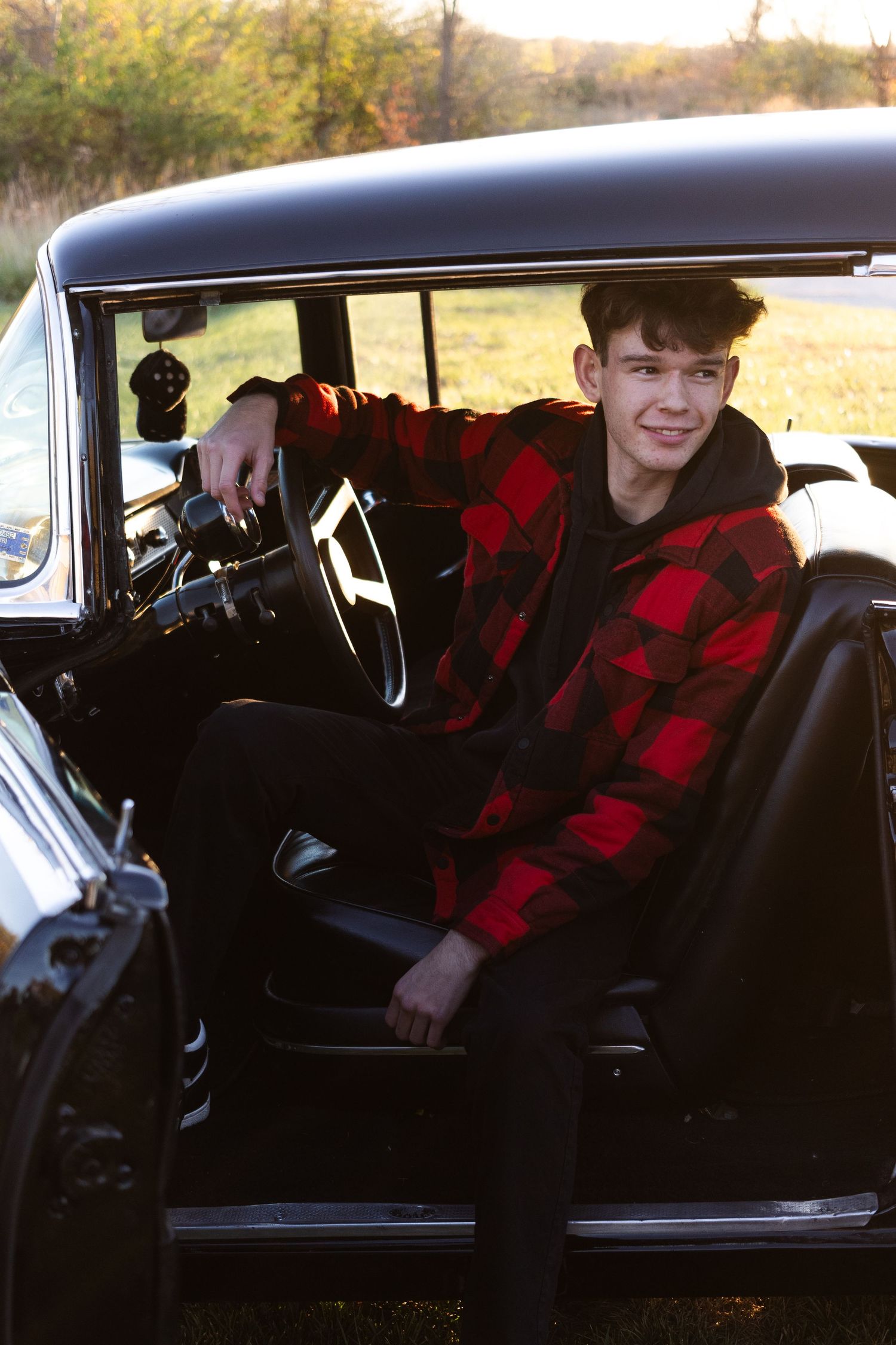 Person in red plaid jacket seated inside classic black car.