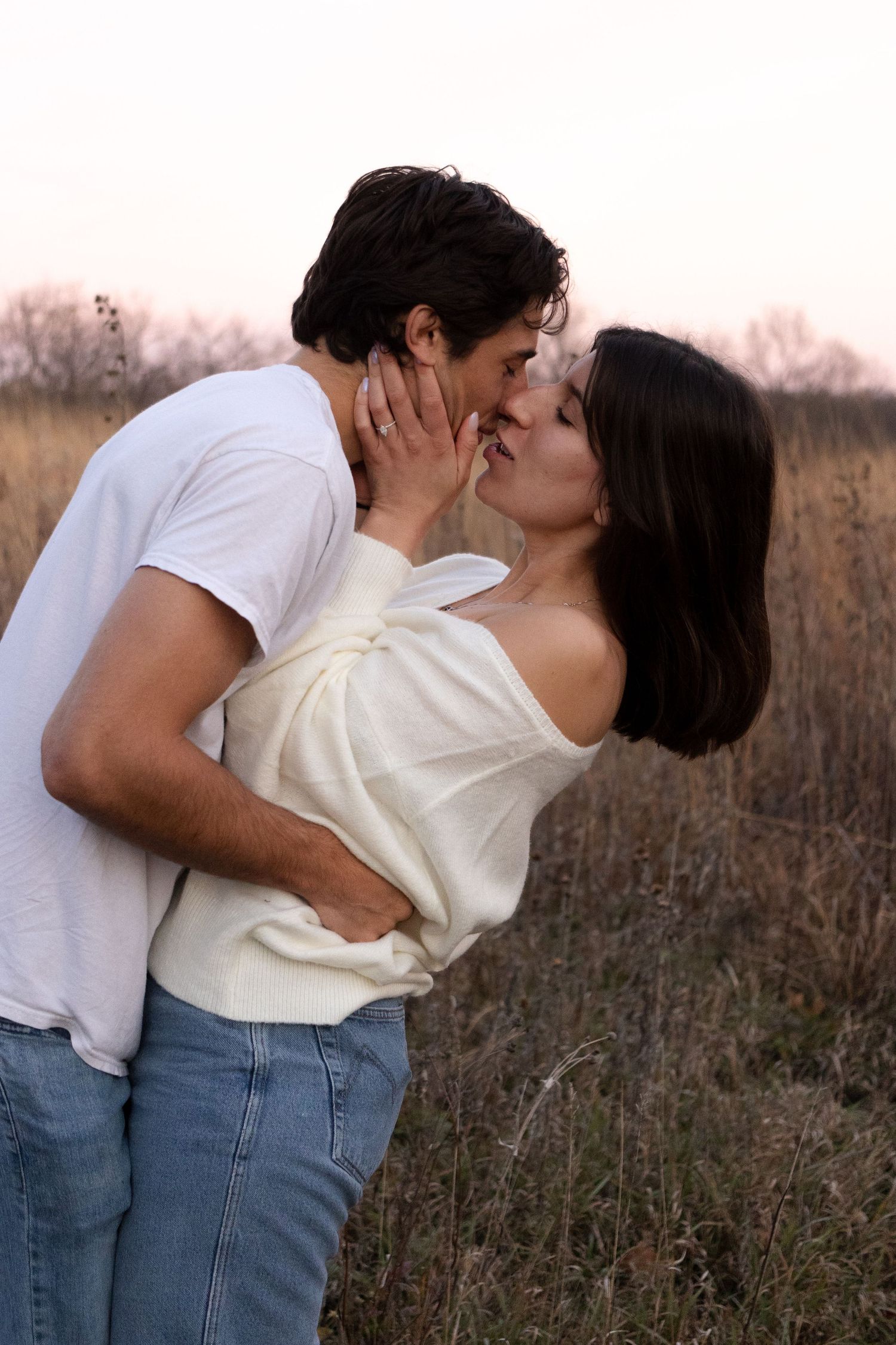 A romantic embrace between a couple in a field during sunset.