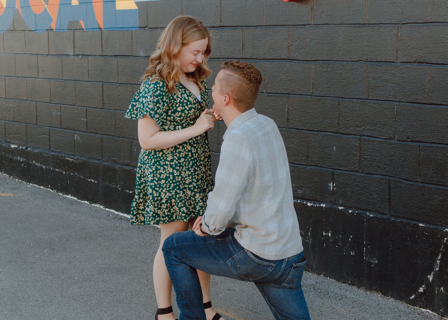 A couple shares a playful dance moment together against a gray brick wall background.