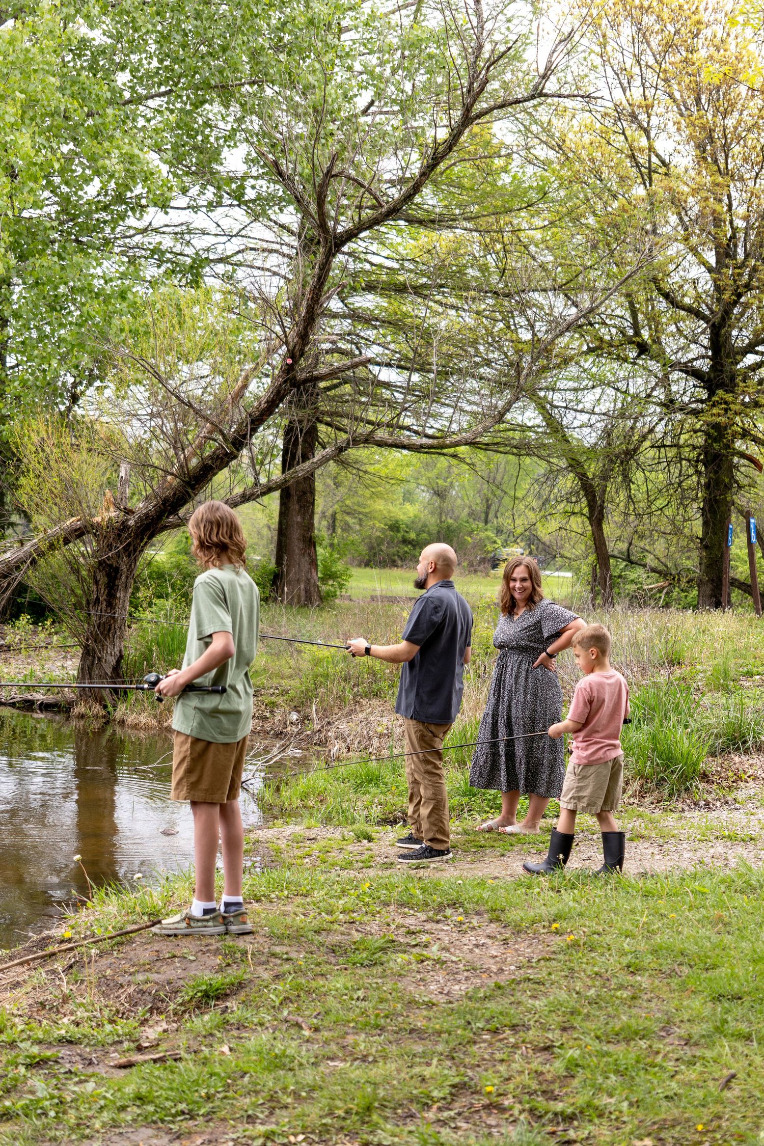Family stands along a creek bank in a wooded area during springtime.