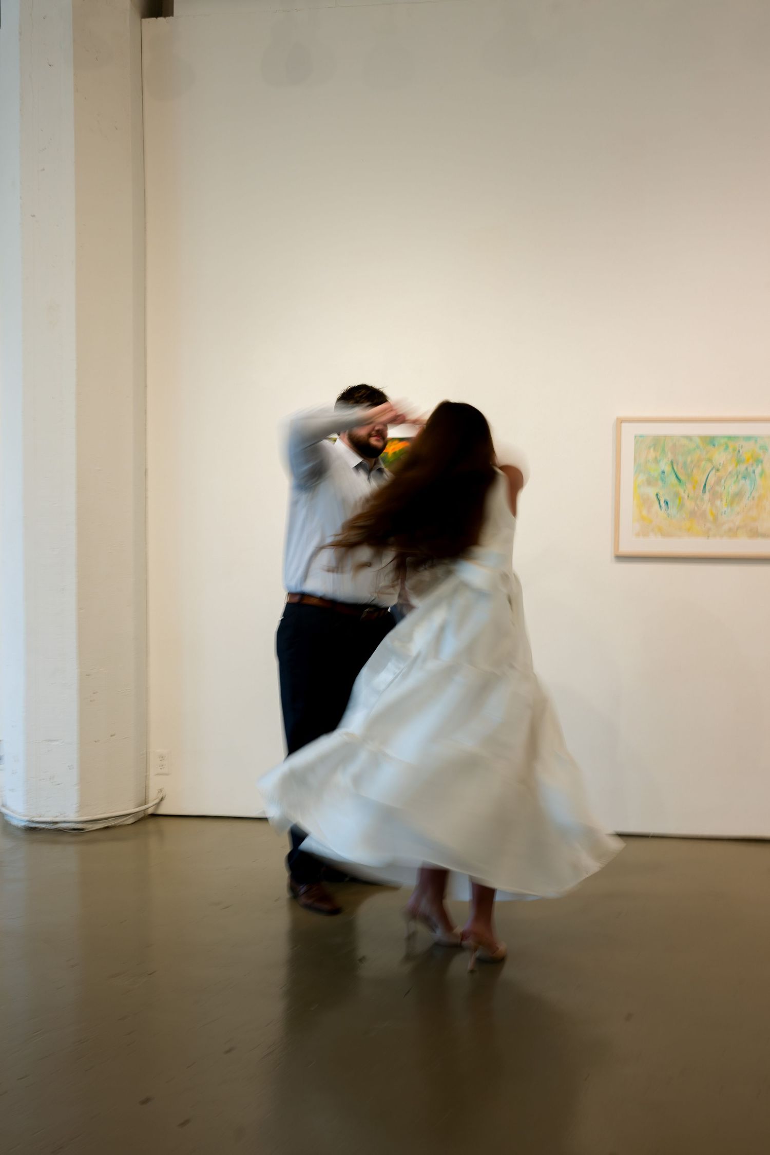 A series of motion-blurred photographs showing dancers performing in a minimalist white gallery space with artwork on walls.