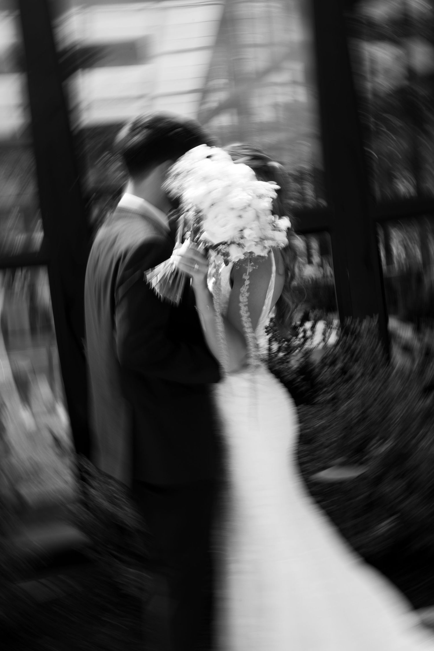 Black and white blurred photo of bride and groom kissing, bride holding white bouquet at wedding ceremony.