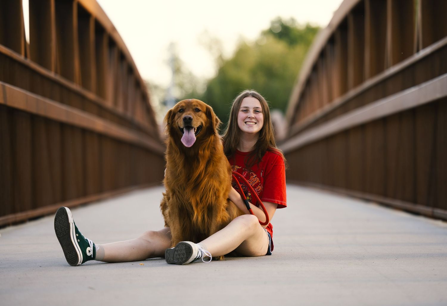 A person in a red sweater and jeans lies on a wooden bridge walkway at sunset.