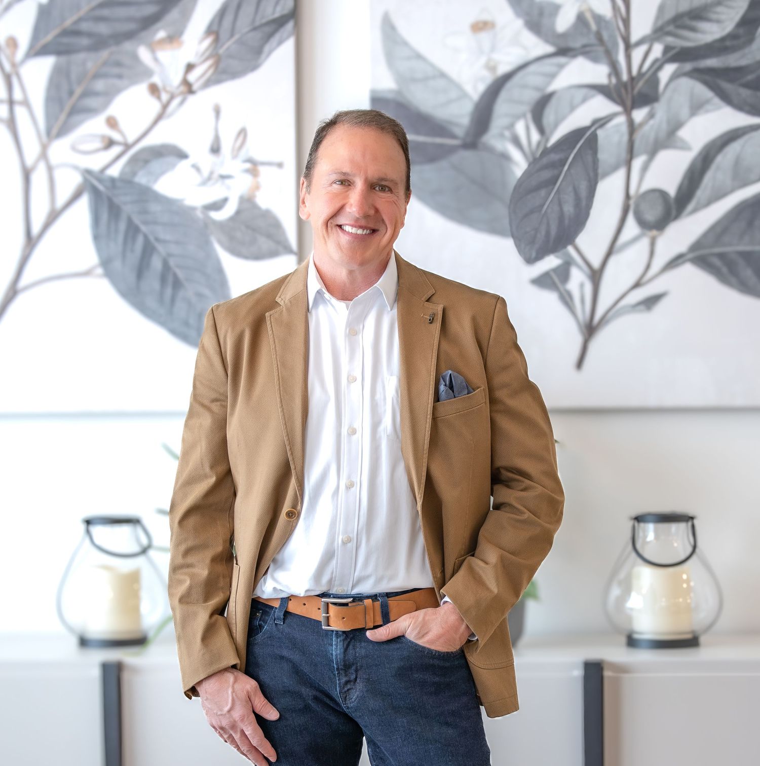 Professional business portrait against white wall with tropical leaf wallpaper in tan blazer and jeans.