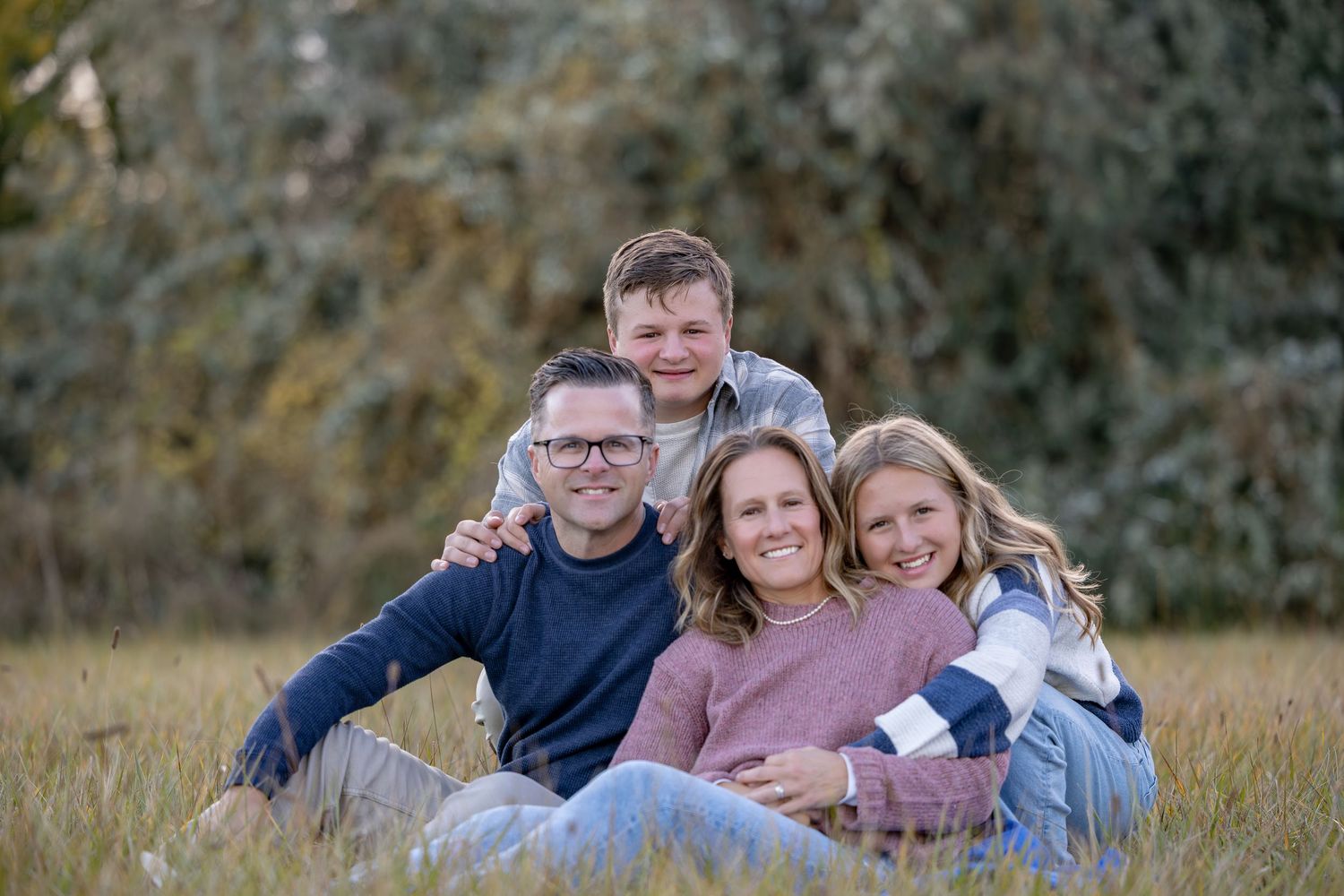 Family group wearing coordinated casual outfits poses together outdoors in autumn setting during photo session.