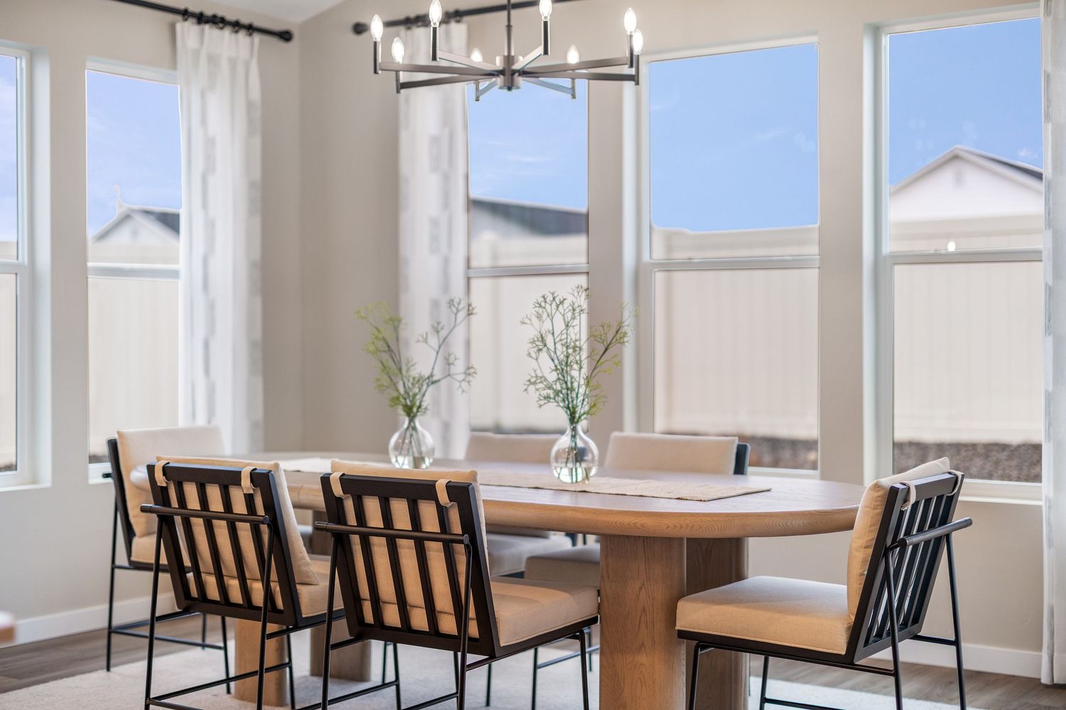 Modern dining room with wooden tables, black chairs, and large windows offering natural light and city views.