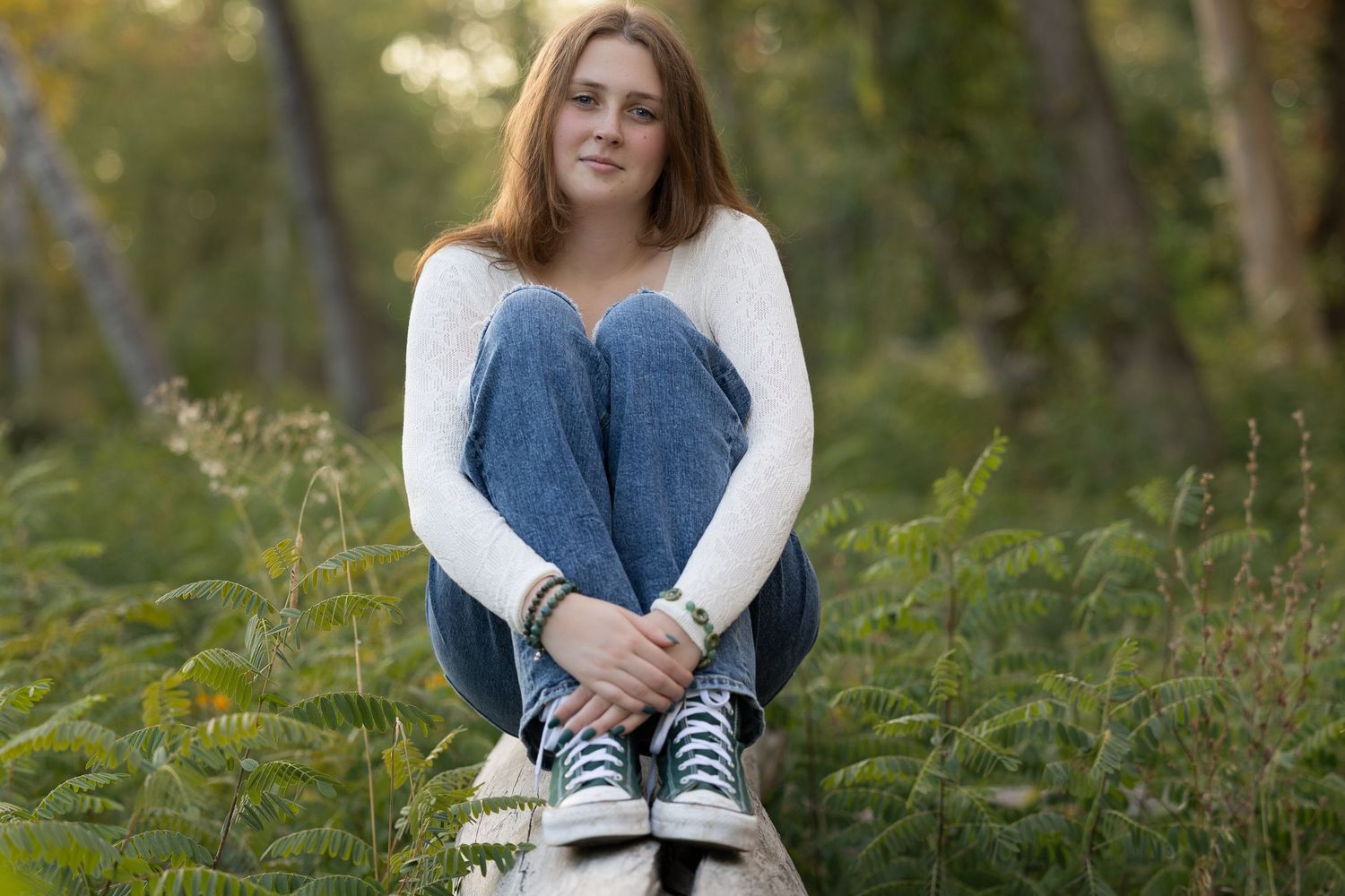 A person in casual attire sits cross-legged on green grass in a sunlit outdoor setting.