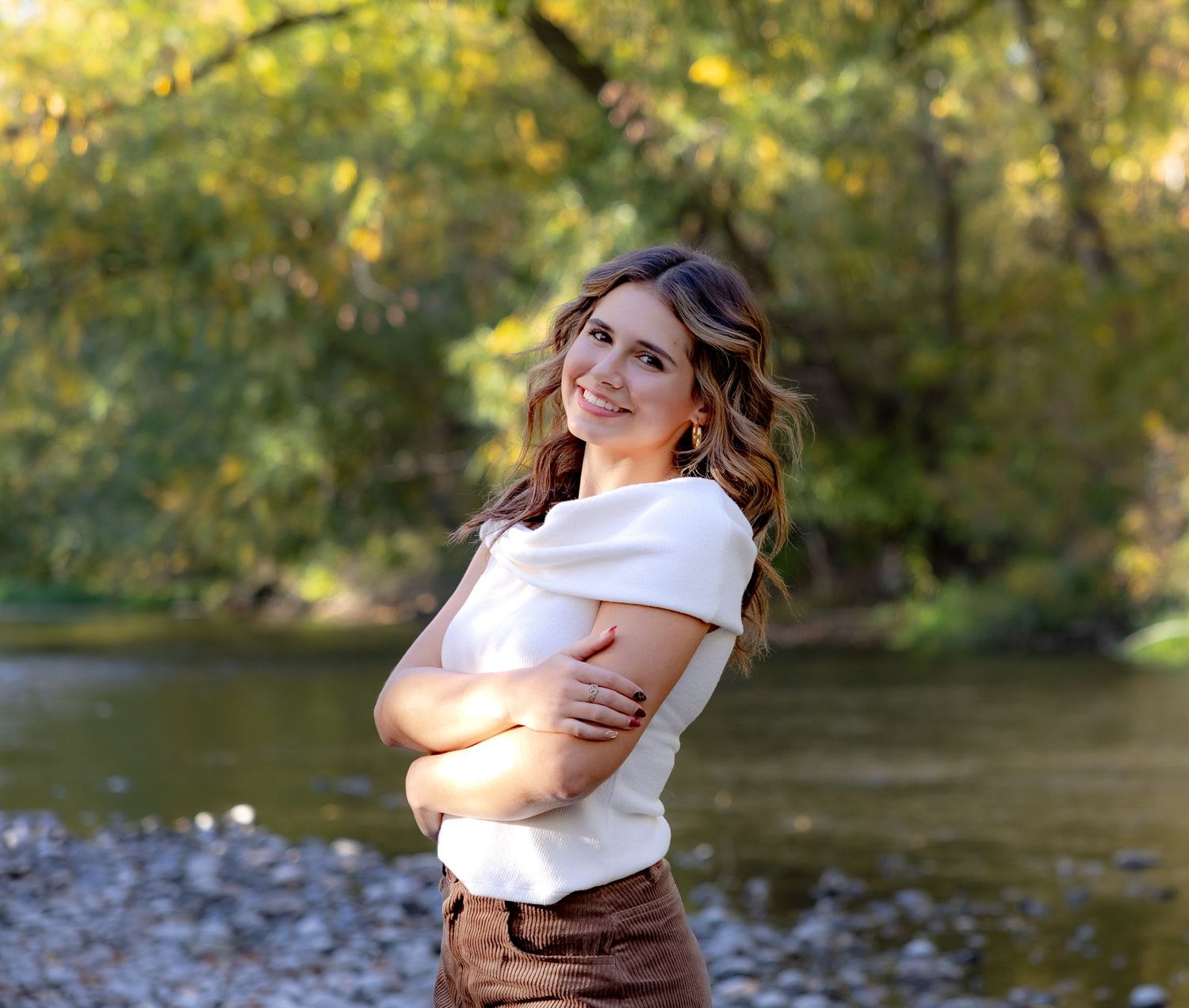 Two people share a joyful embrace by a sunlit river with autumn foliage in the background.
