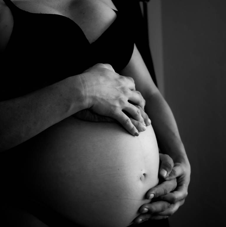 Black and white artistic maternity photo showing hands gently cradling a pregnant belly.