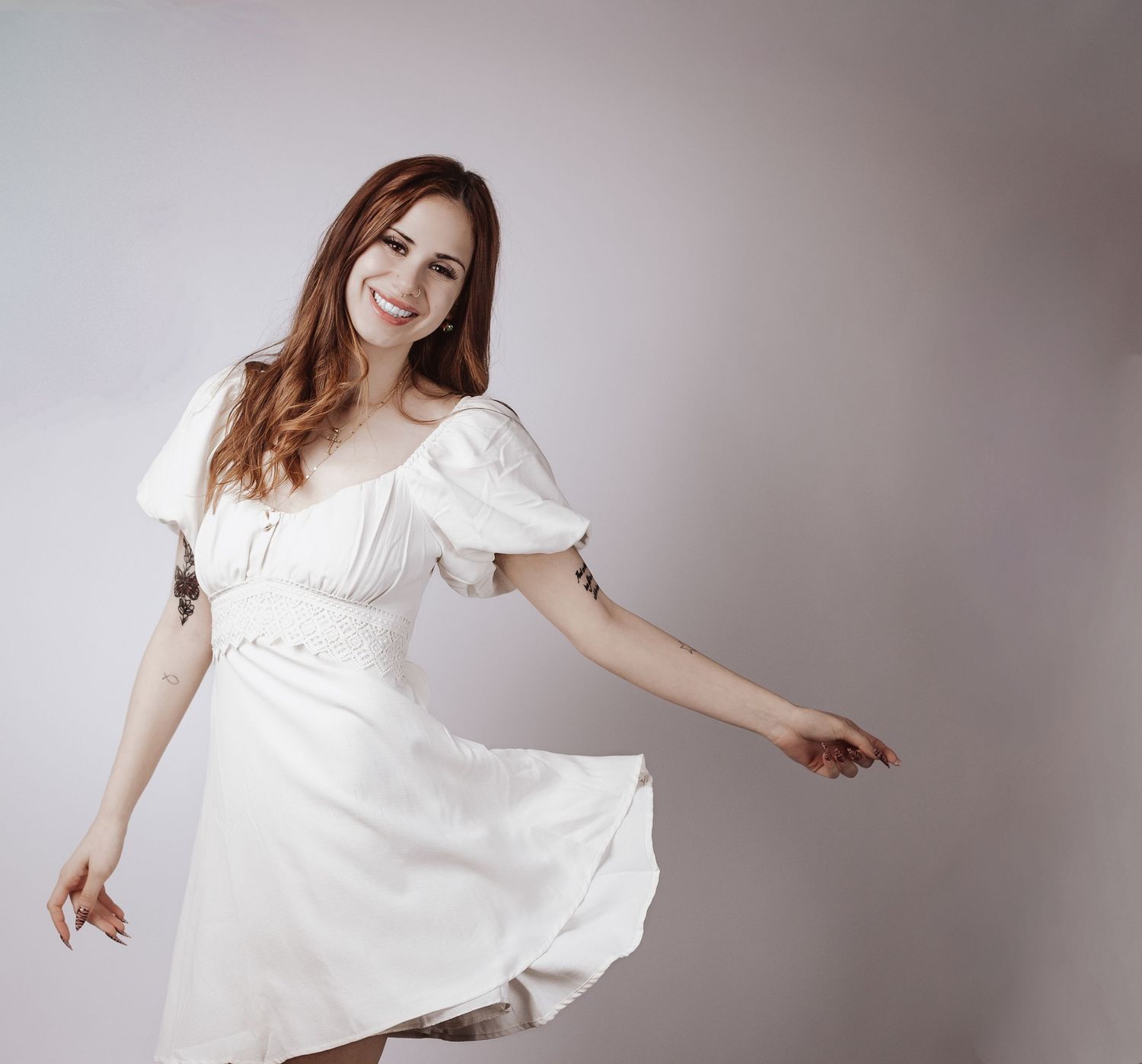 Woman in flowing white dress twirls gracefully against grey backdrop in artistic fashion photoshoot sequence.