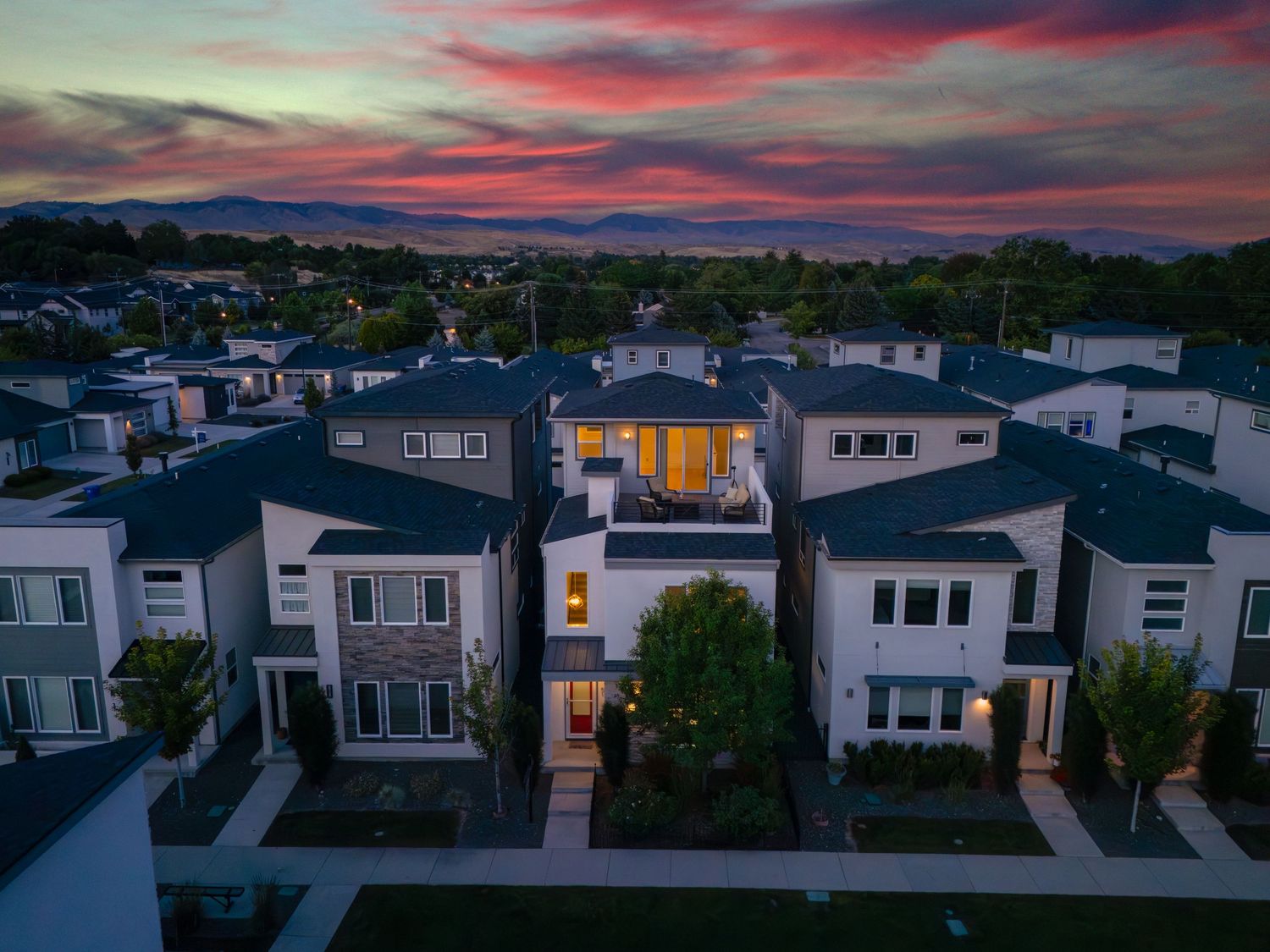 Aerial sunset view of modern suburban neighborhood with illuminated homes and mountain backdrop.