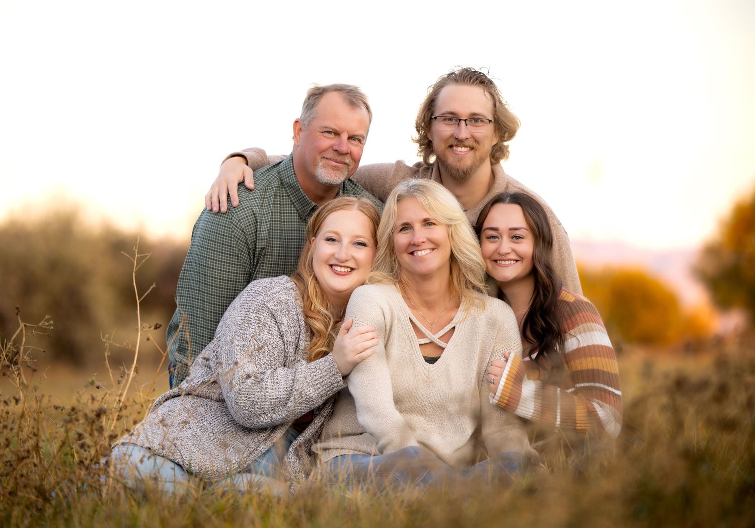A family sits together on grass during golden hour sunset for outdoor portrait photography.