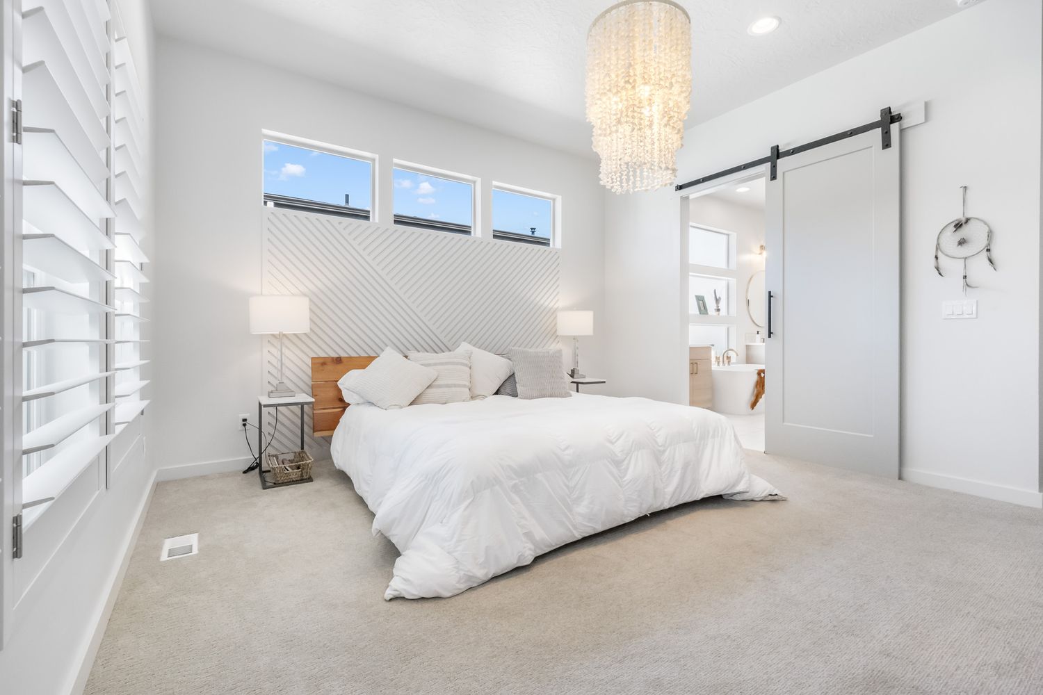 Modern white bedroom interior with luxury crystal chandelier, plush carpet and sliding barn door against bright decor.