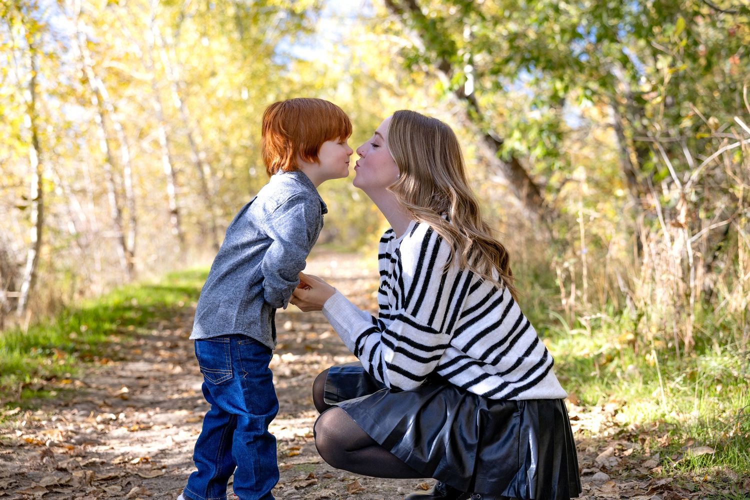 A family sits together on a fallen tree trunk in a wooded area during an outdoor photo session.