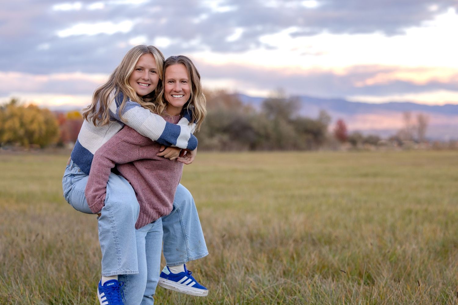 A couple embraces in a golden field at sunset with mountains in the background.