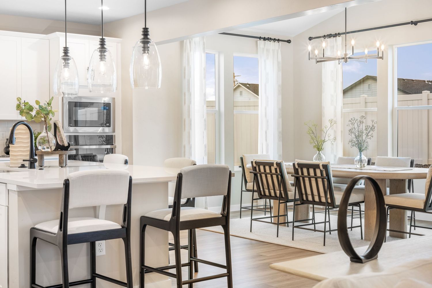 Modern open concept kitchen and dining area with white countertops, pendant lighting and black bar stools.