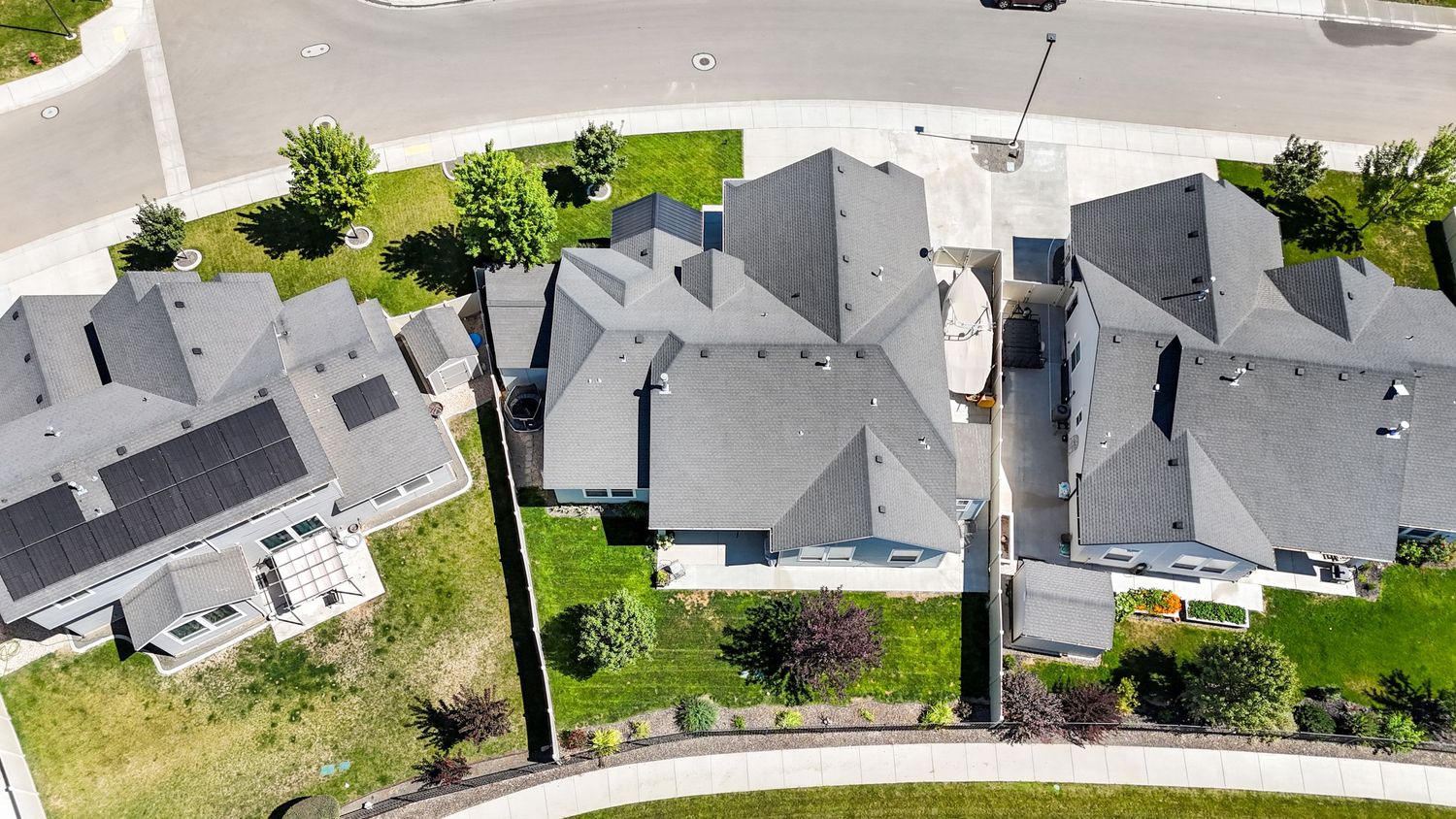 Aerial view of modern suburban neighborhood with gray rooftops and green lawns on a sunny day.