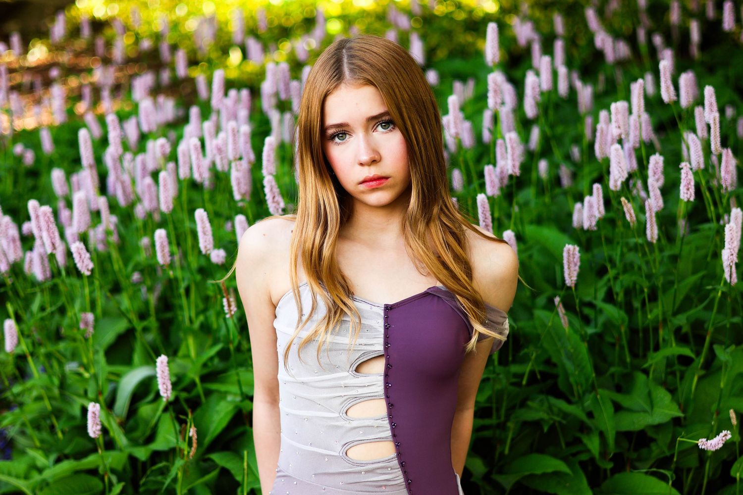 Dance-inspired portrait among purple flowers wearing a two-toned dress.