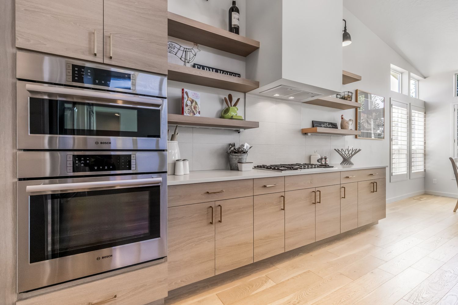 Modern kitchen design with light wood cabinets, built-in appliances, and sleek stainless steel hardware along white walls.