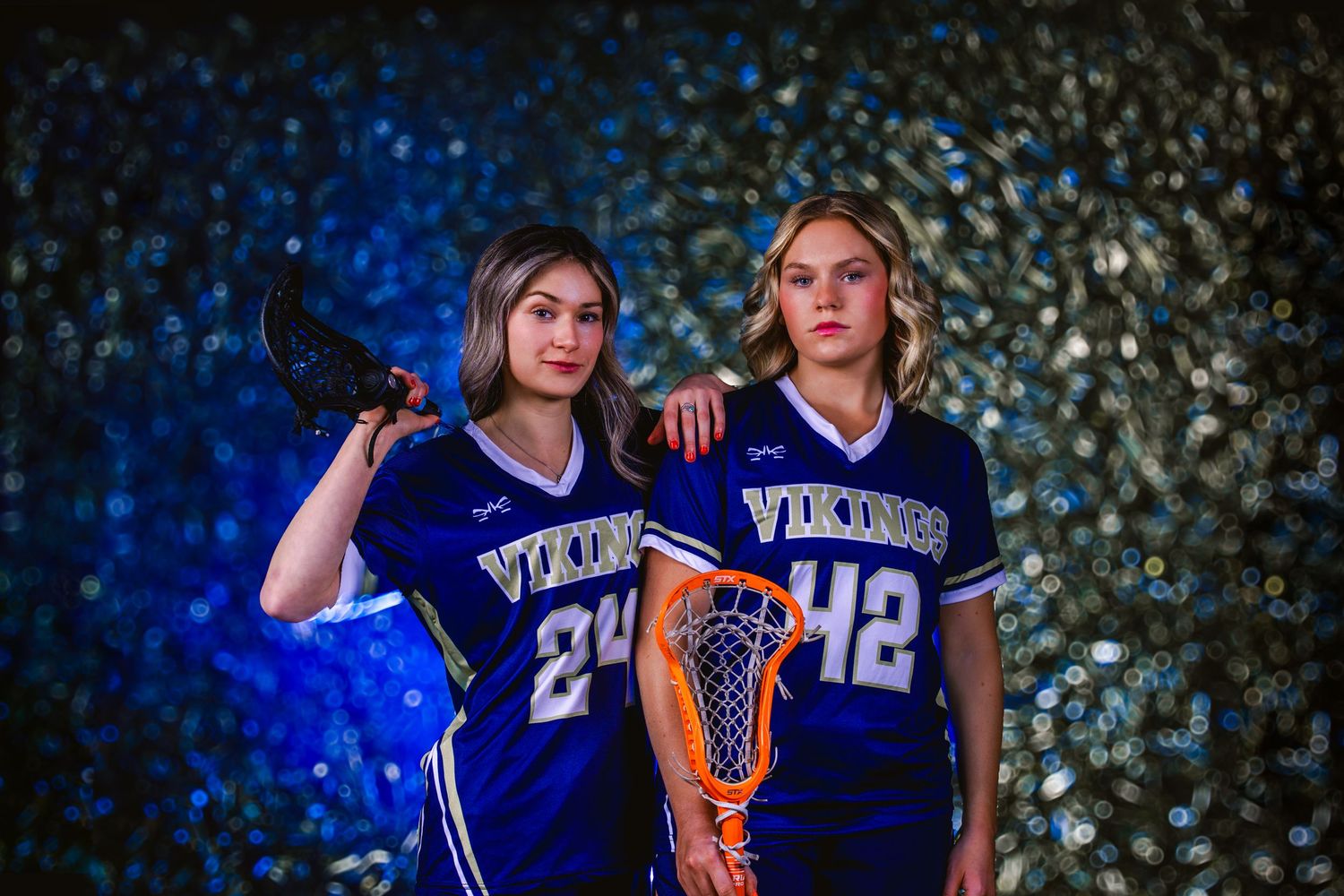 Two basketball players in blue jerseys pose together with glittering lights in the background.
